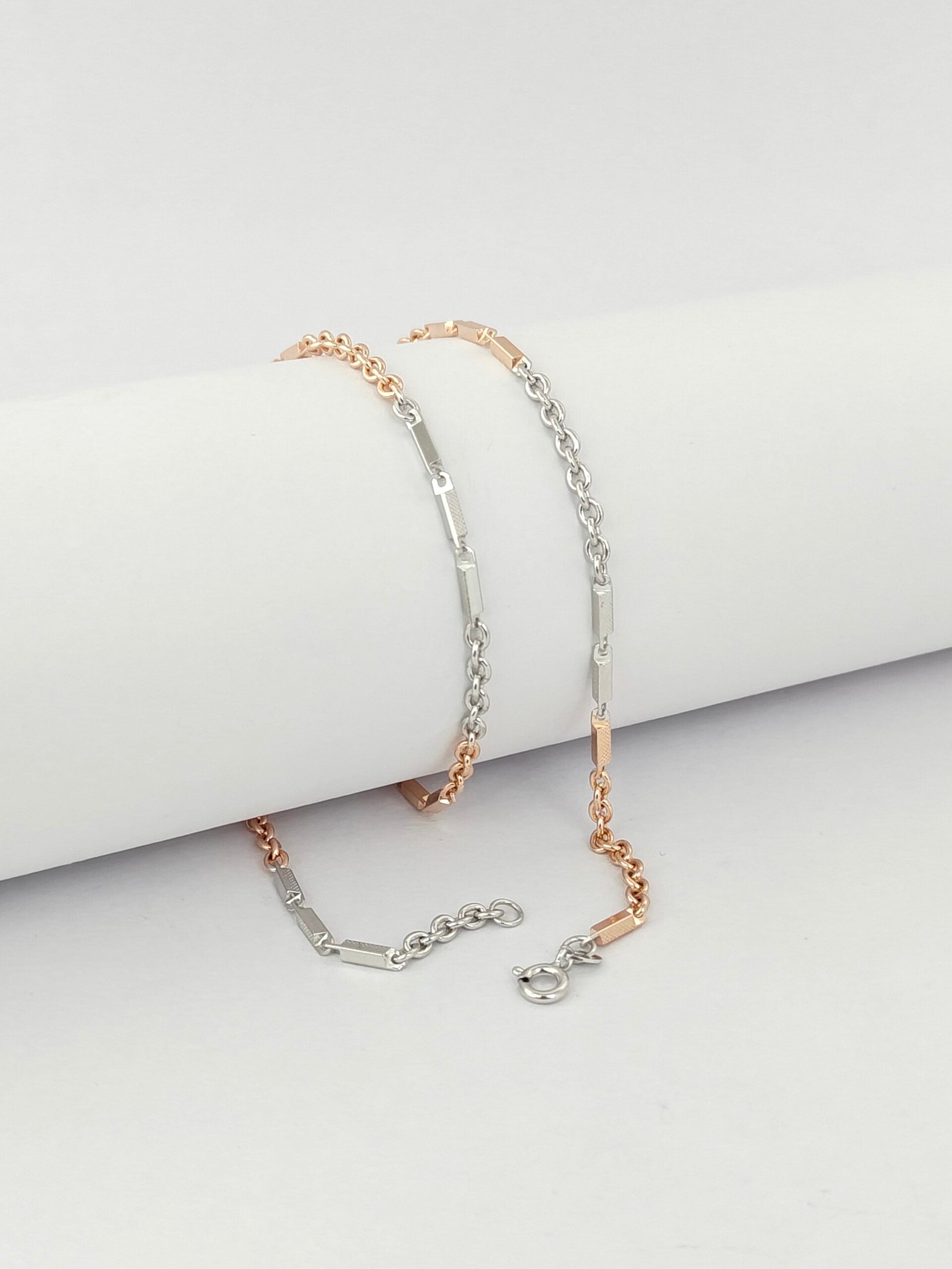 Two gold and silver chain bracelets on a light gray surface