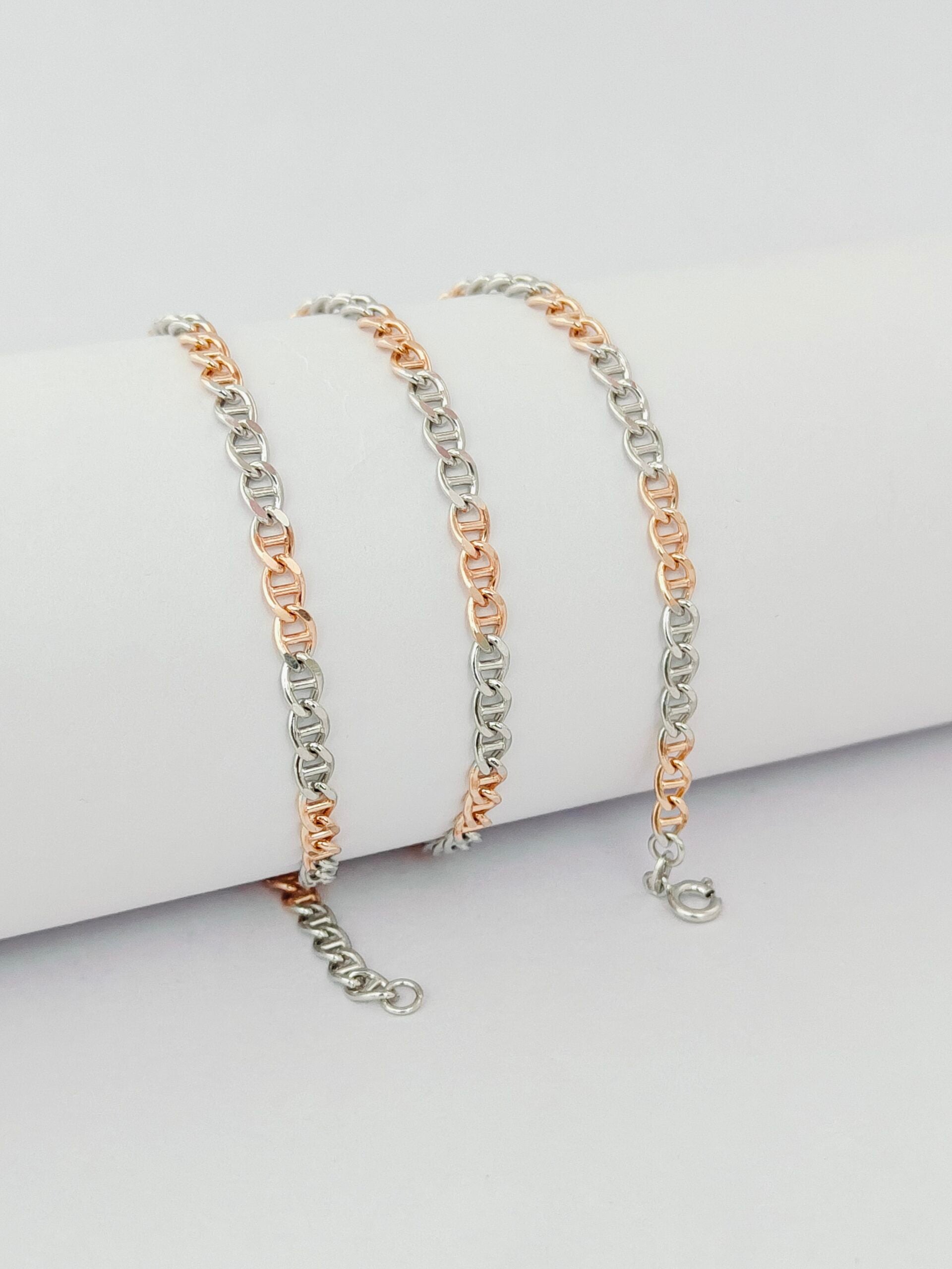 Three gold and silver chain bracelets on a light gray surface