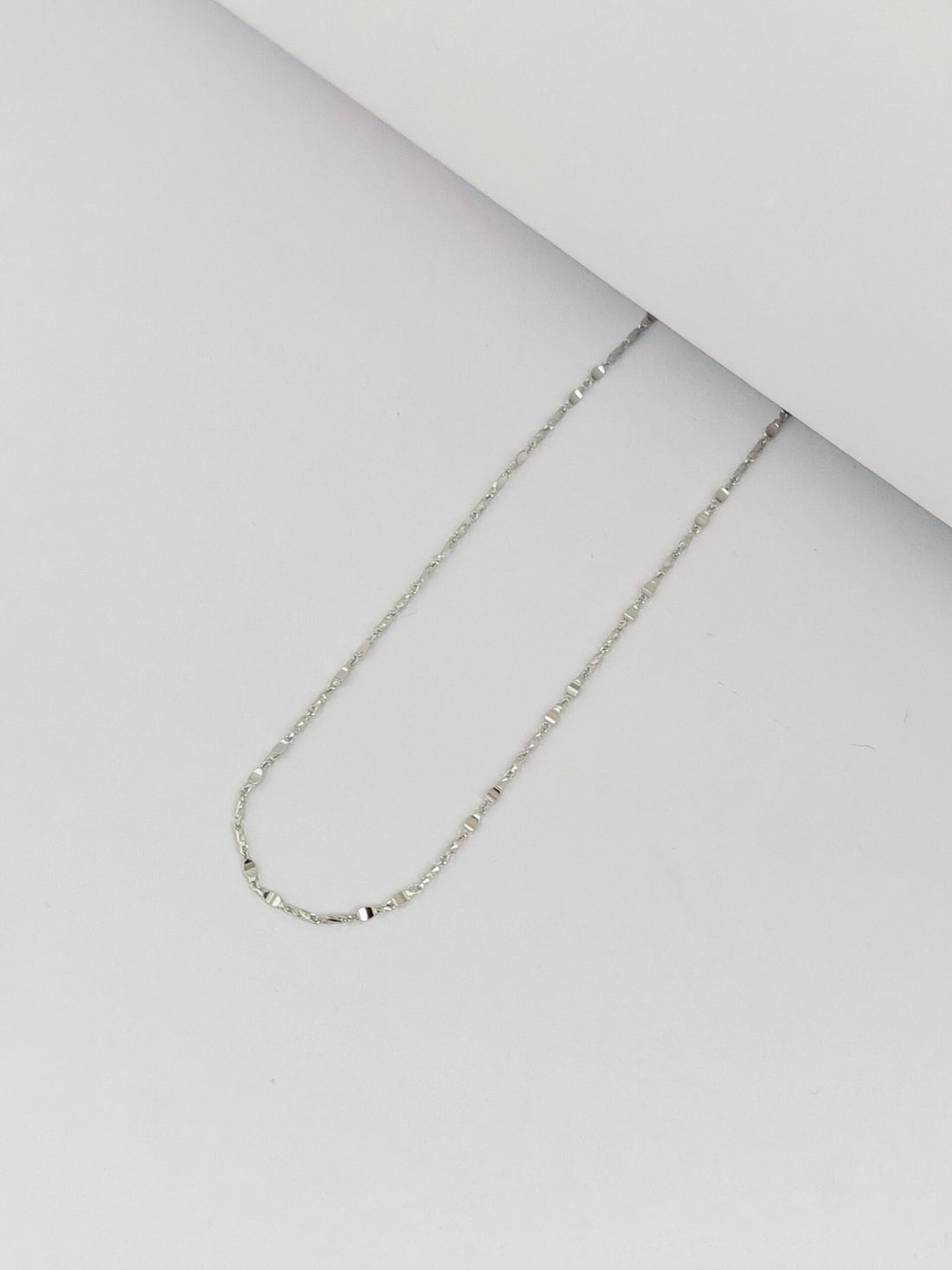 Silver chain necklace on a light gray surface