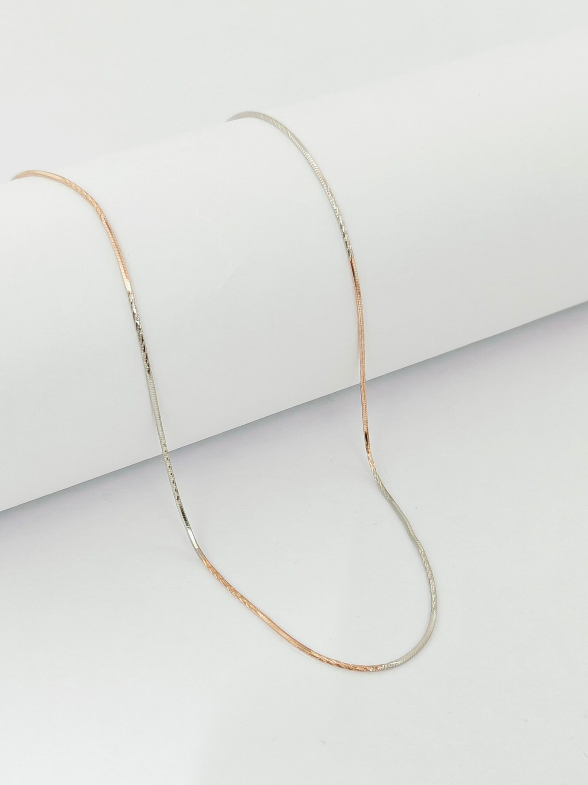 Thin gold chain necklace on a light gray background