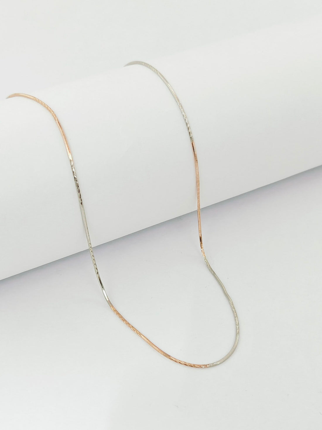 Thin gold chain necklace on a light gray background