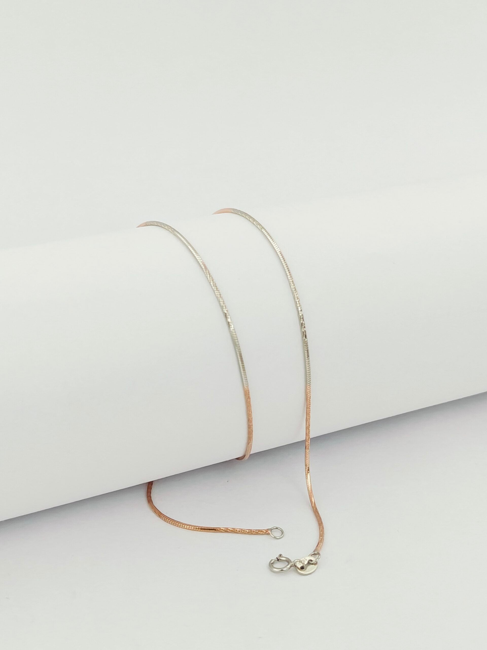 Delicate gold necklace on a light gray surface with a white background