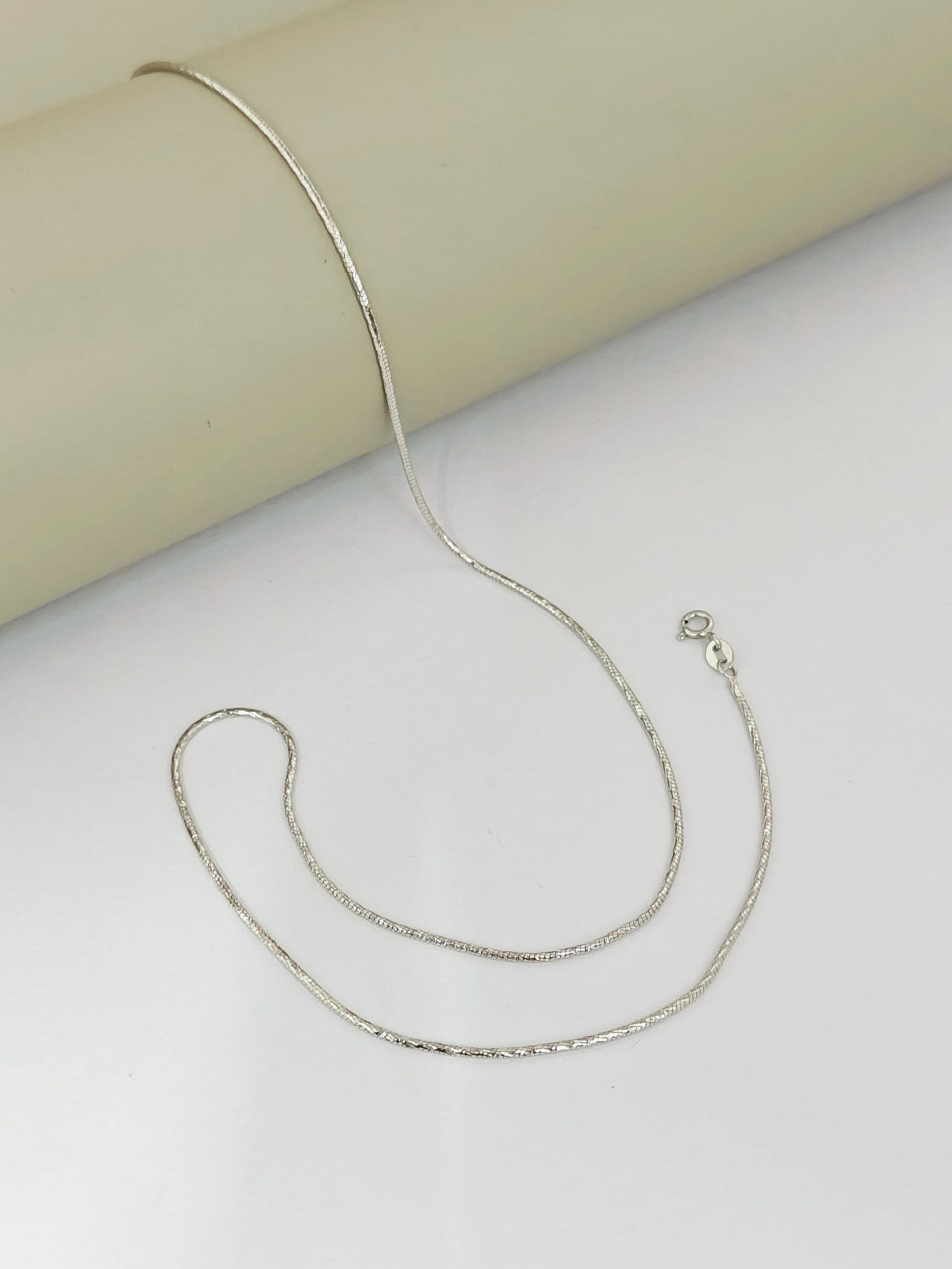 Silver necklace on a light gray surface with a beige background