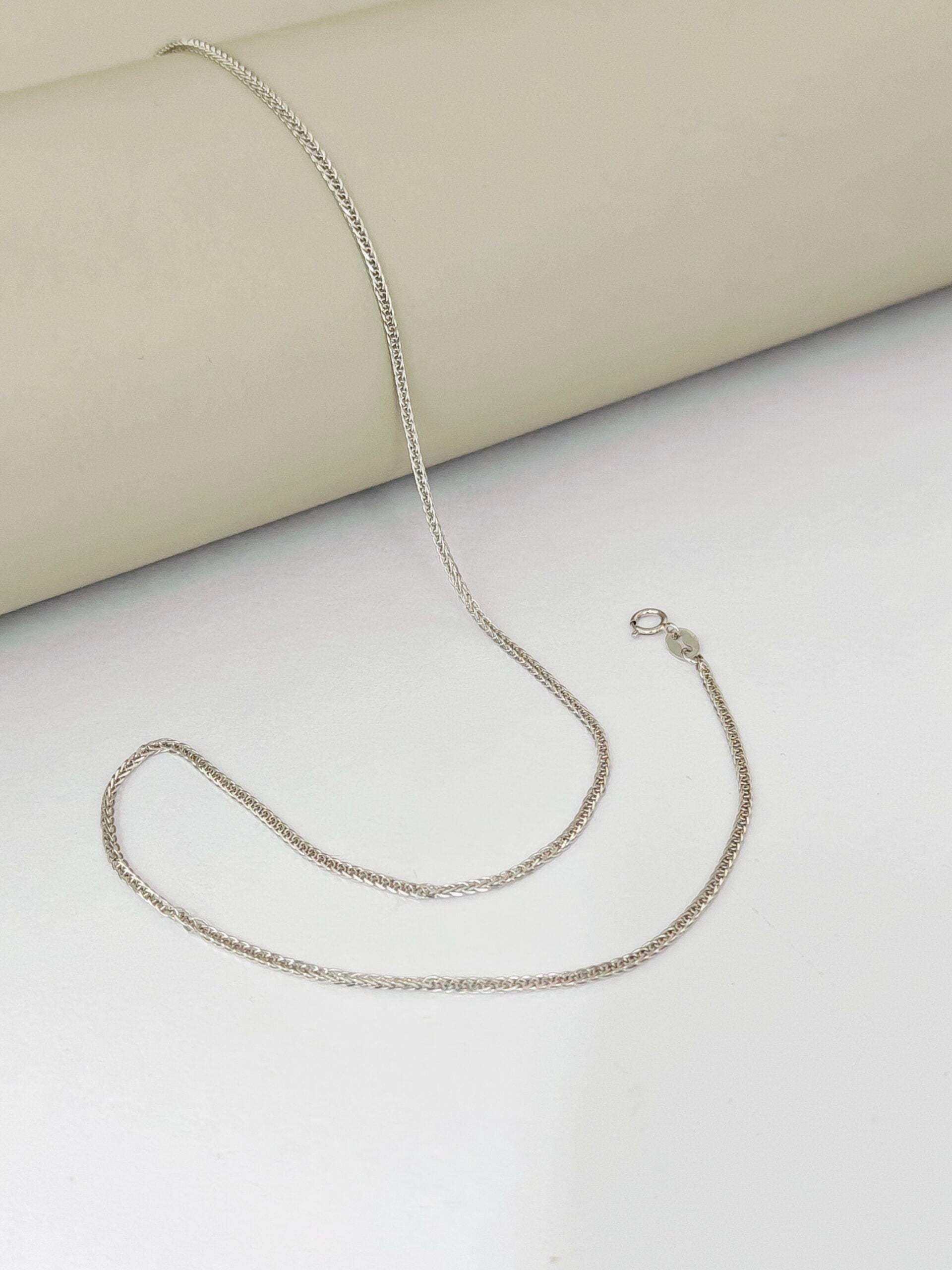 Silver chain necklace on a light gray surface with a beige fabric background