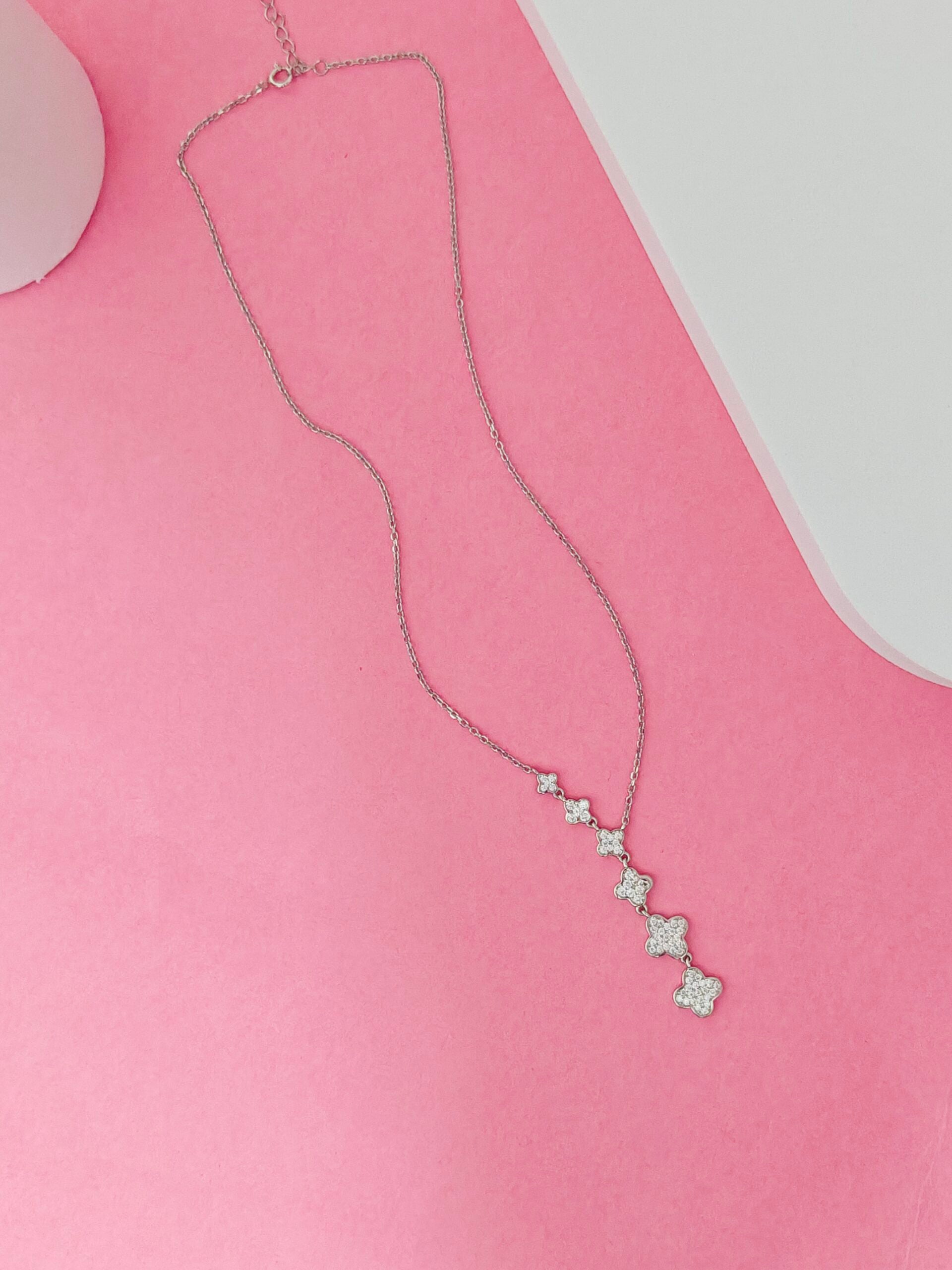 Silver necklace with star-shaped pendants on a pink surface