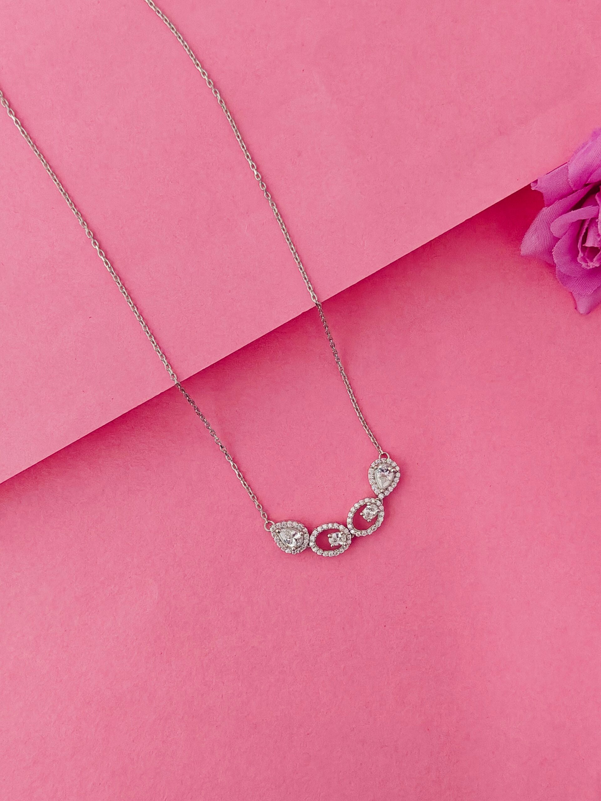 Necklace with three heart-shaped gemstones on a pink background