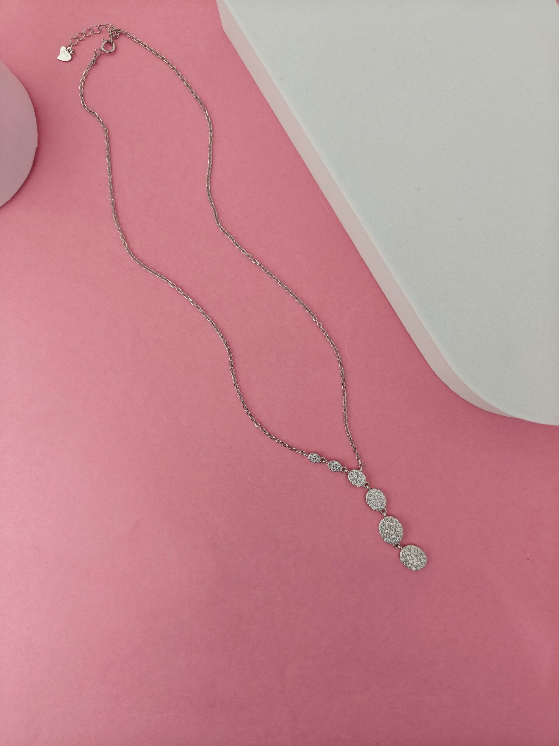 Silver necklace with heart pendant on a pink surface