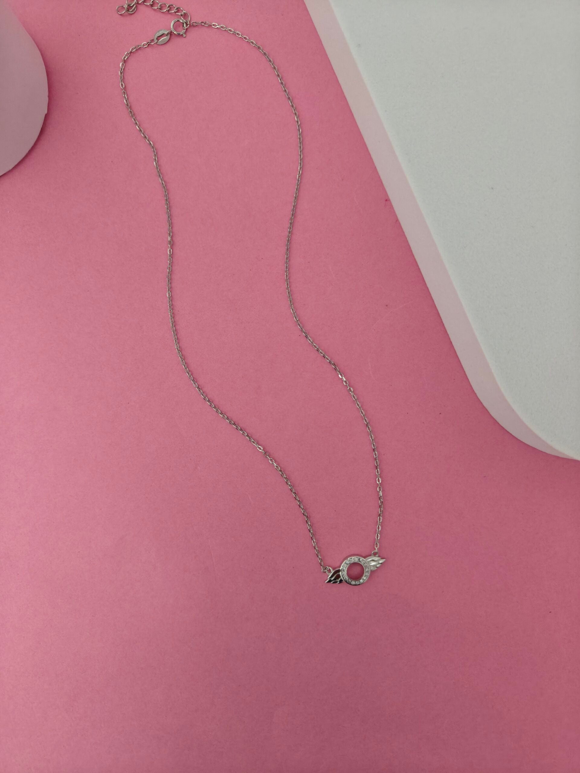 Silver necklace with a small pendant on a pink surface