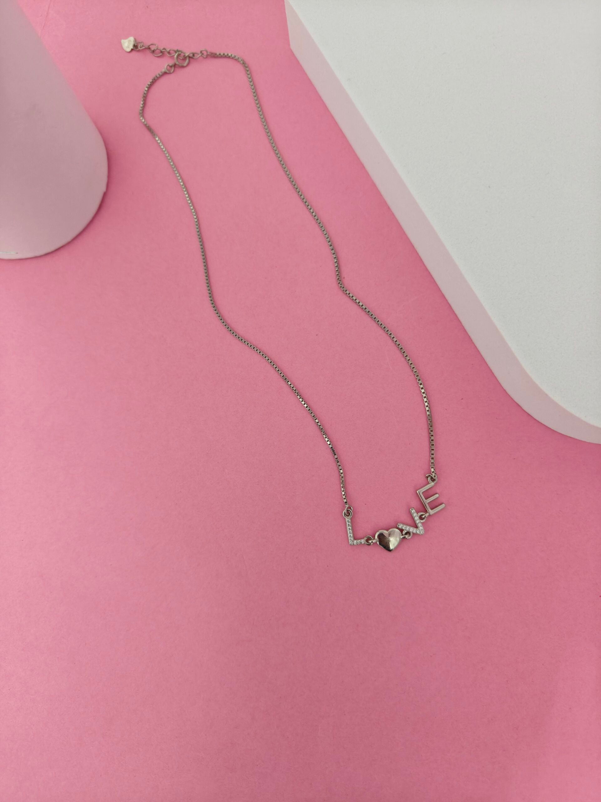 Necklace with 'LOVE' pendant on a pink surface
