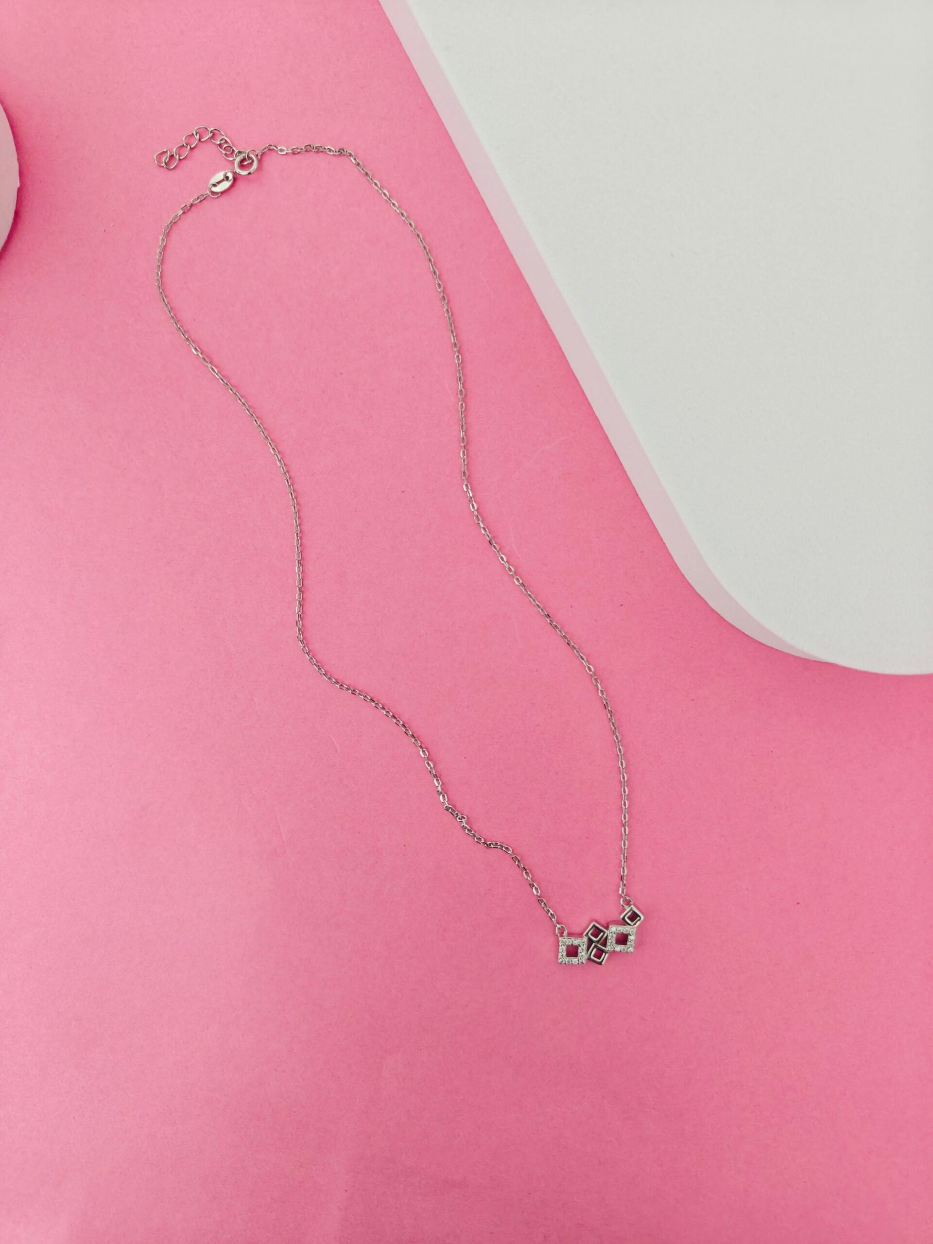 Silver necklace with small pendants on a pink surface