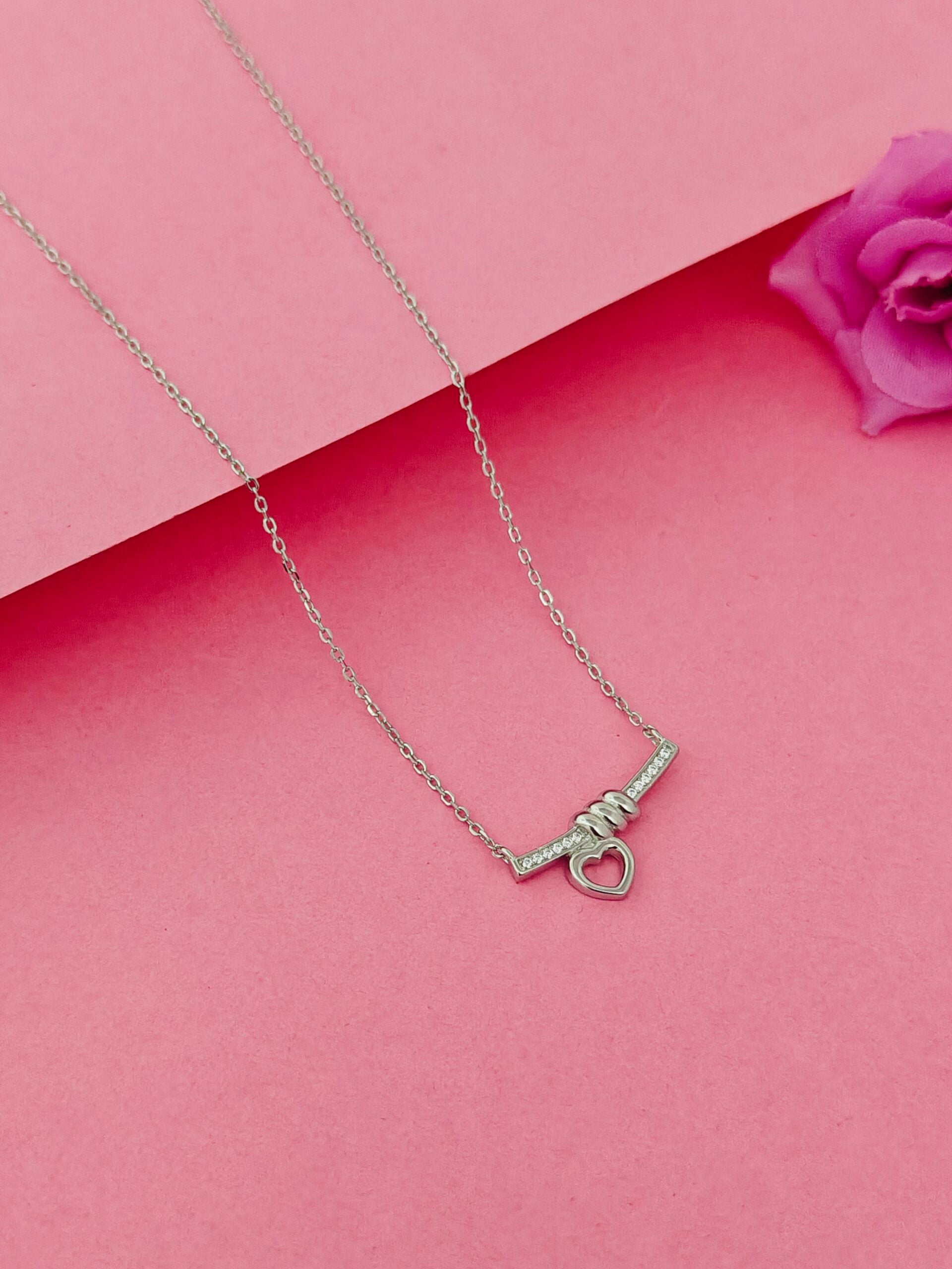 Silver necklace with a heart-shaped pendant on a pink background