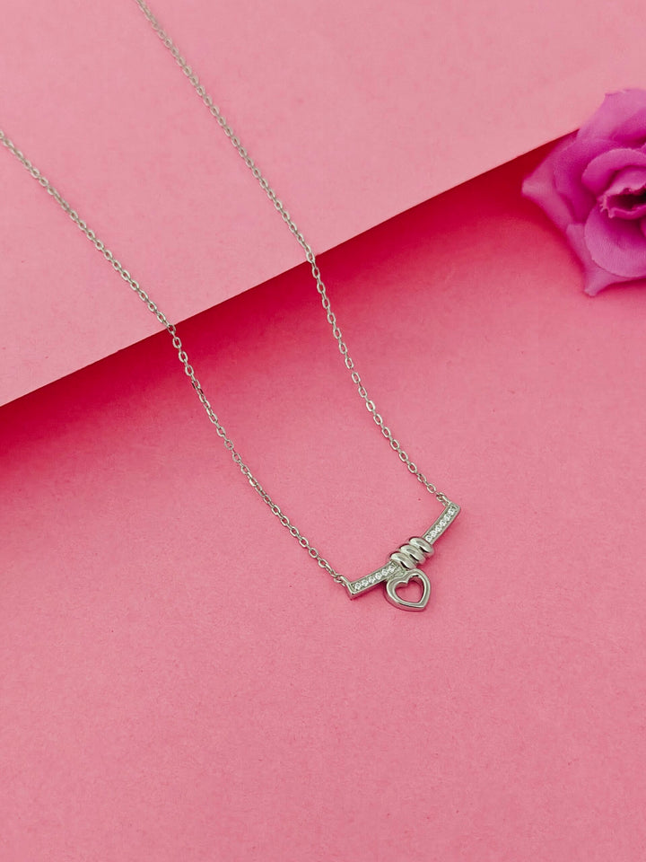 Silver necklace with a heart-shaped pendant on a pink background