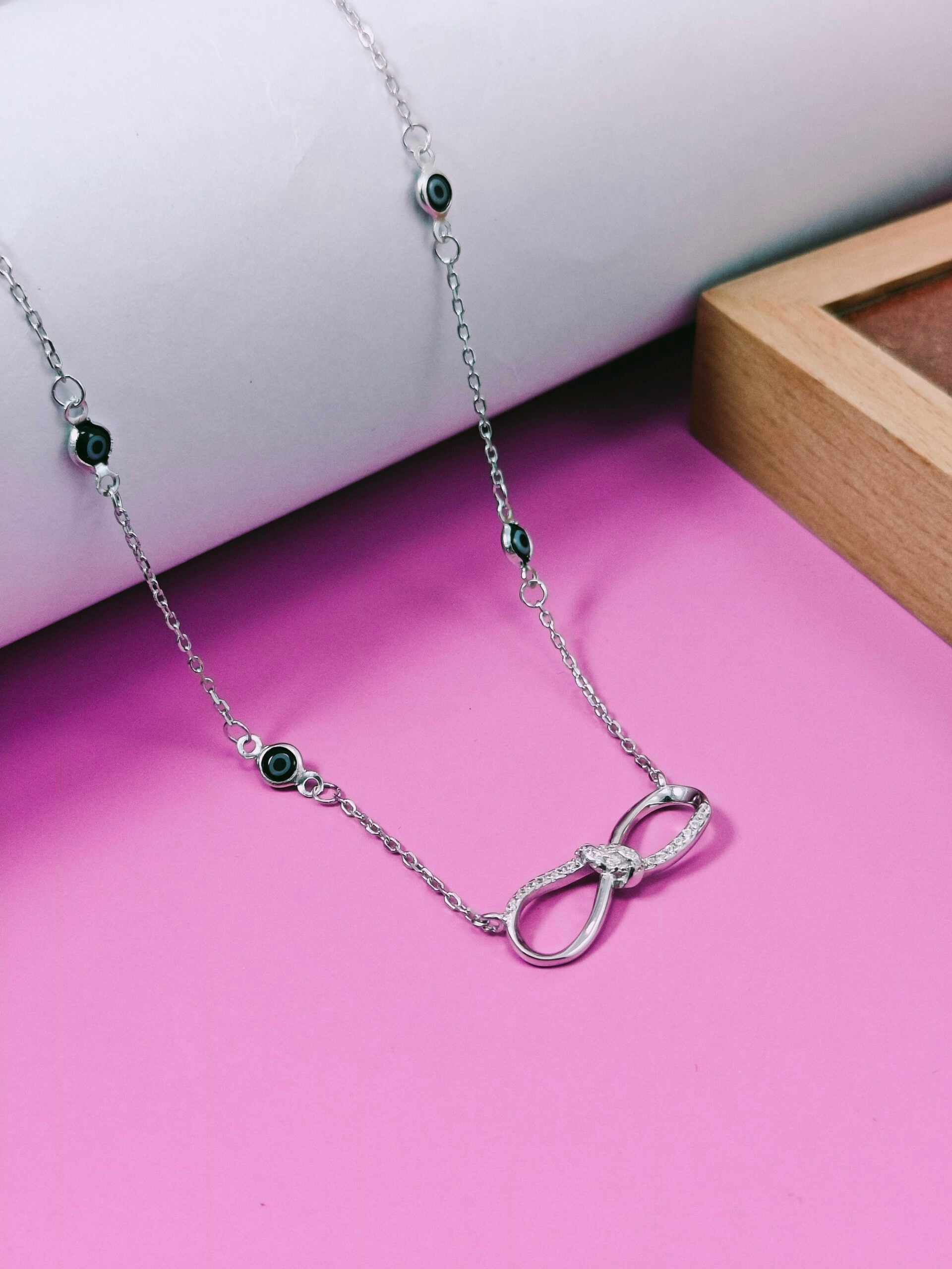 Silver necklace with green gemstones on a pink surface