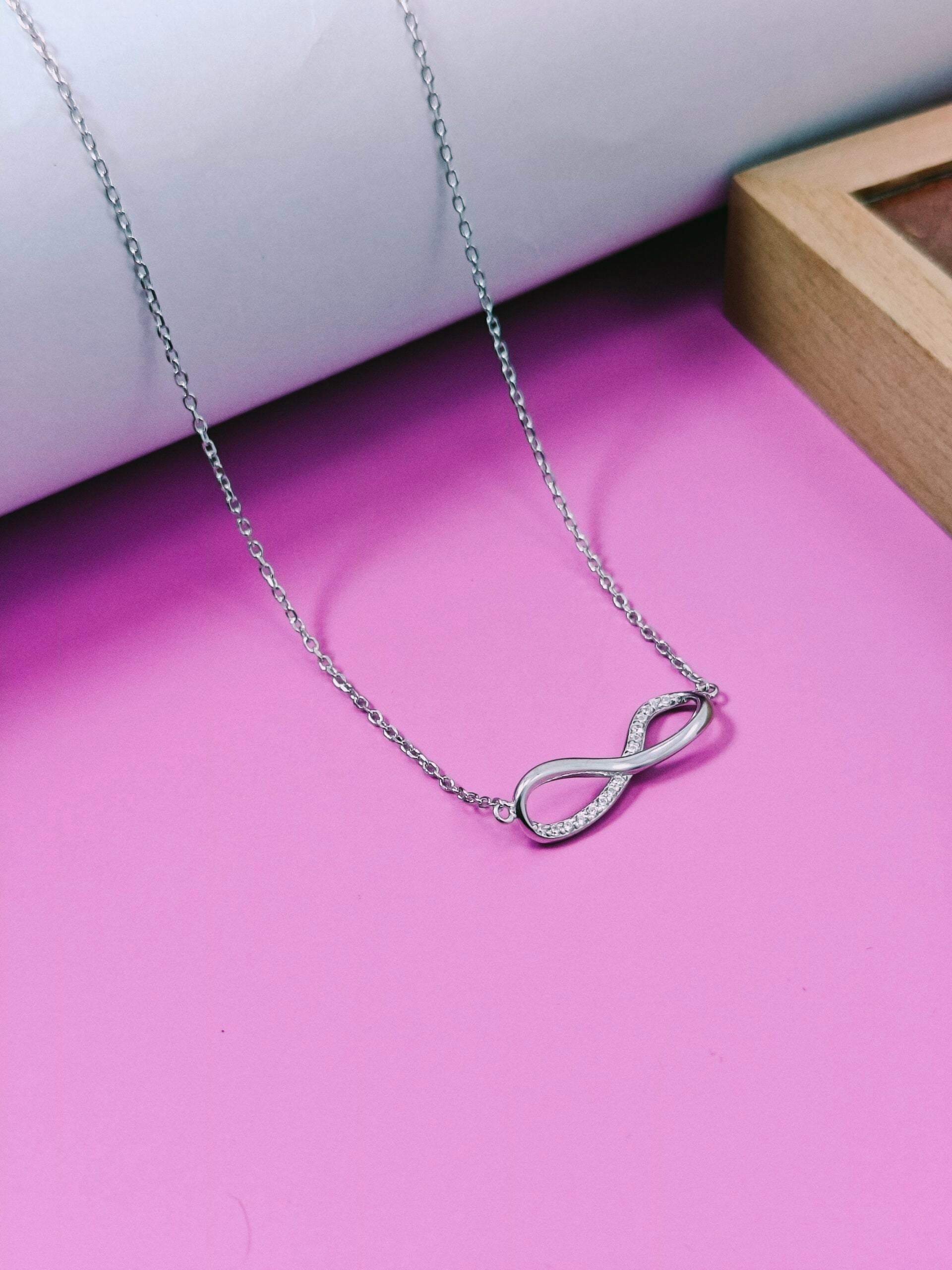 Silver infinity necklace on a pink surface