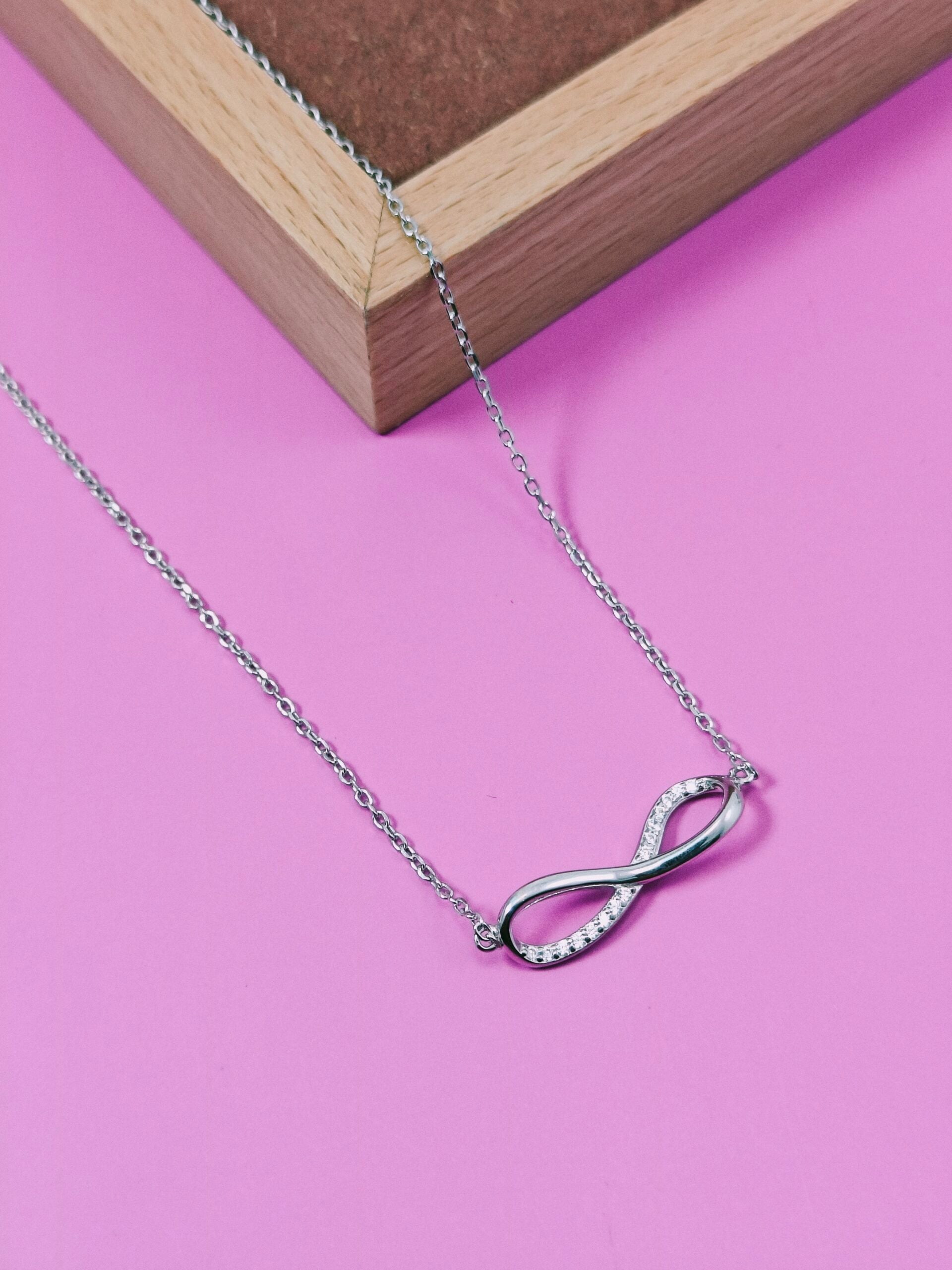 Silver infinity necklace on a pink background