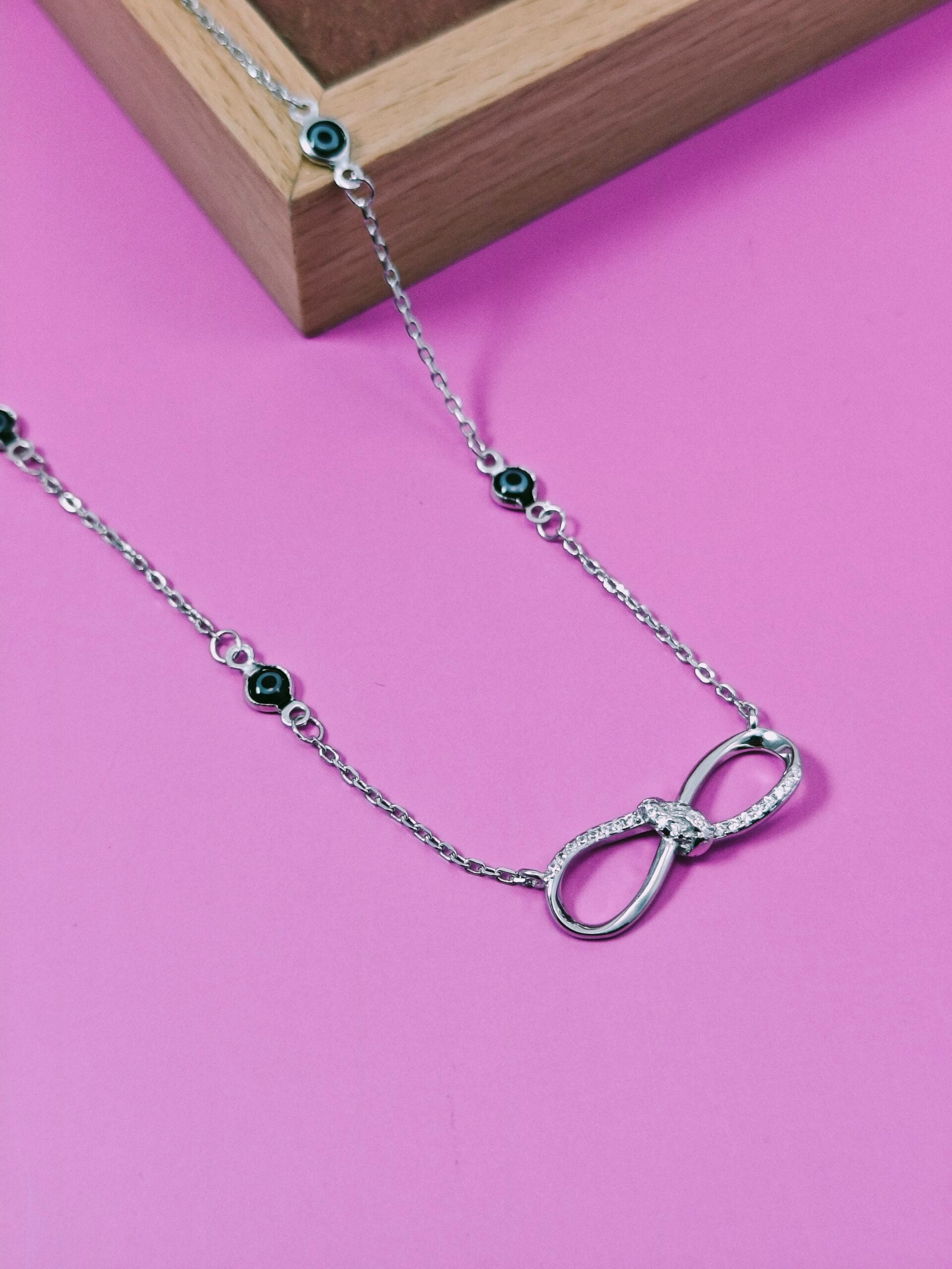 Silver necklace with an infinity symbol pendant on a pink background
