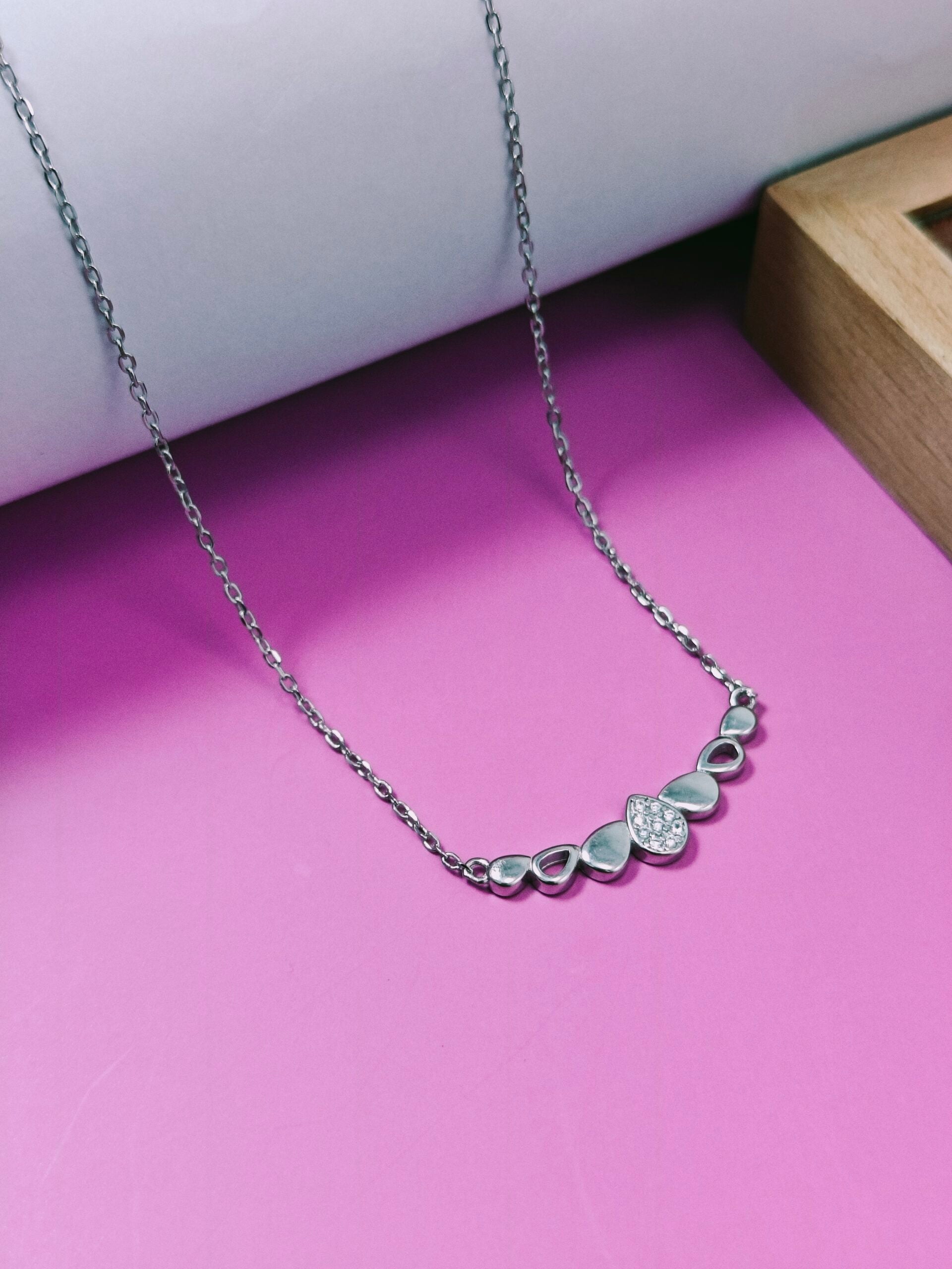 Silver necklace with floral designs on a pink surface