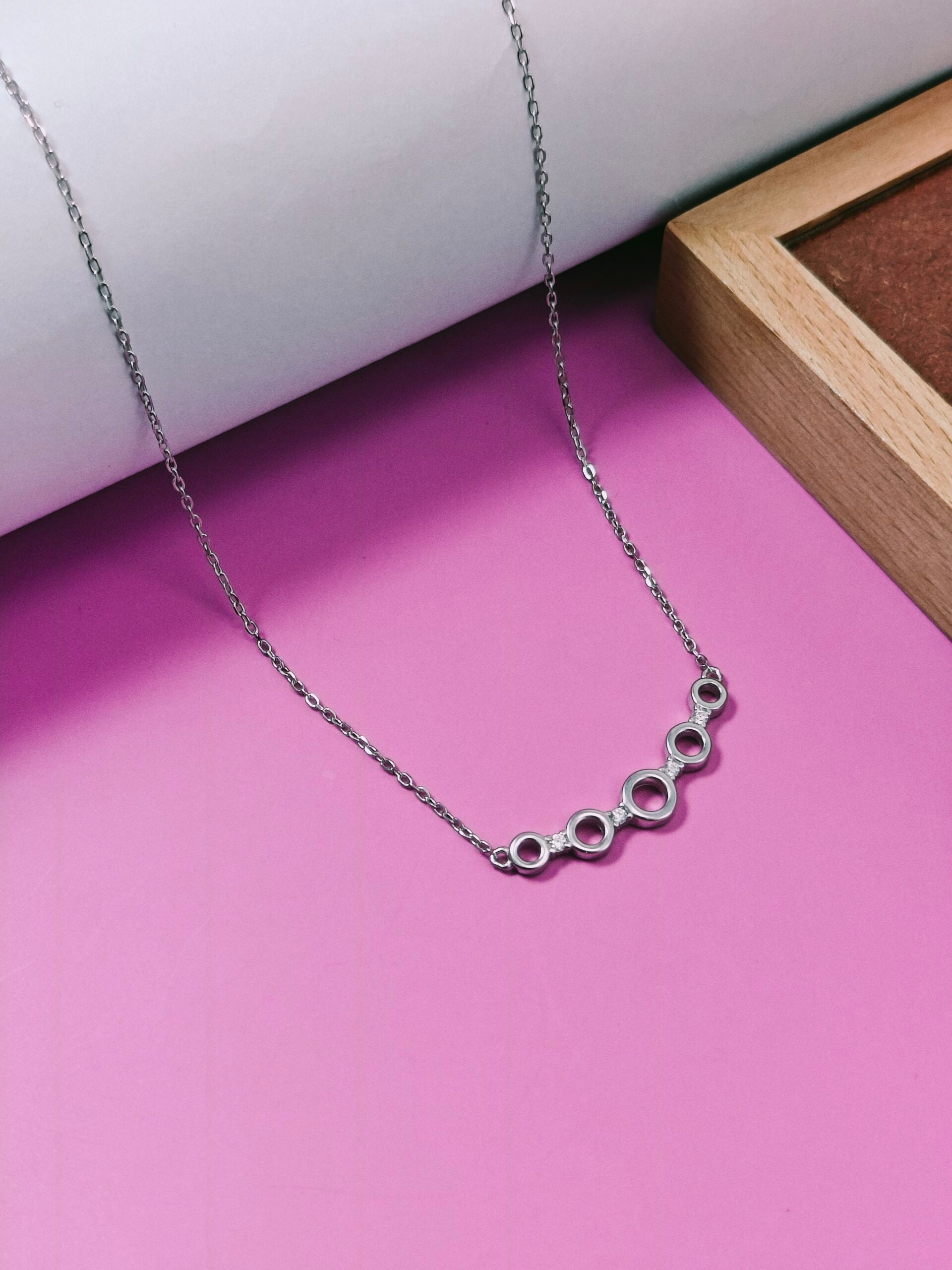 Silver necklace with circular links on a pink surface