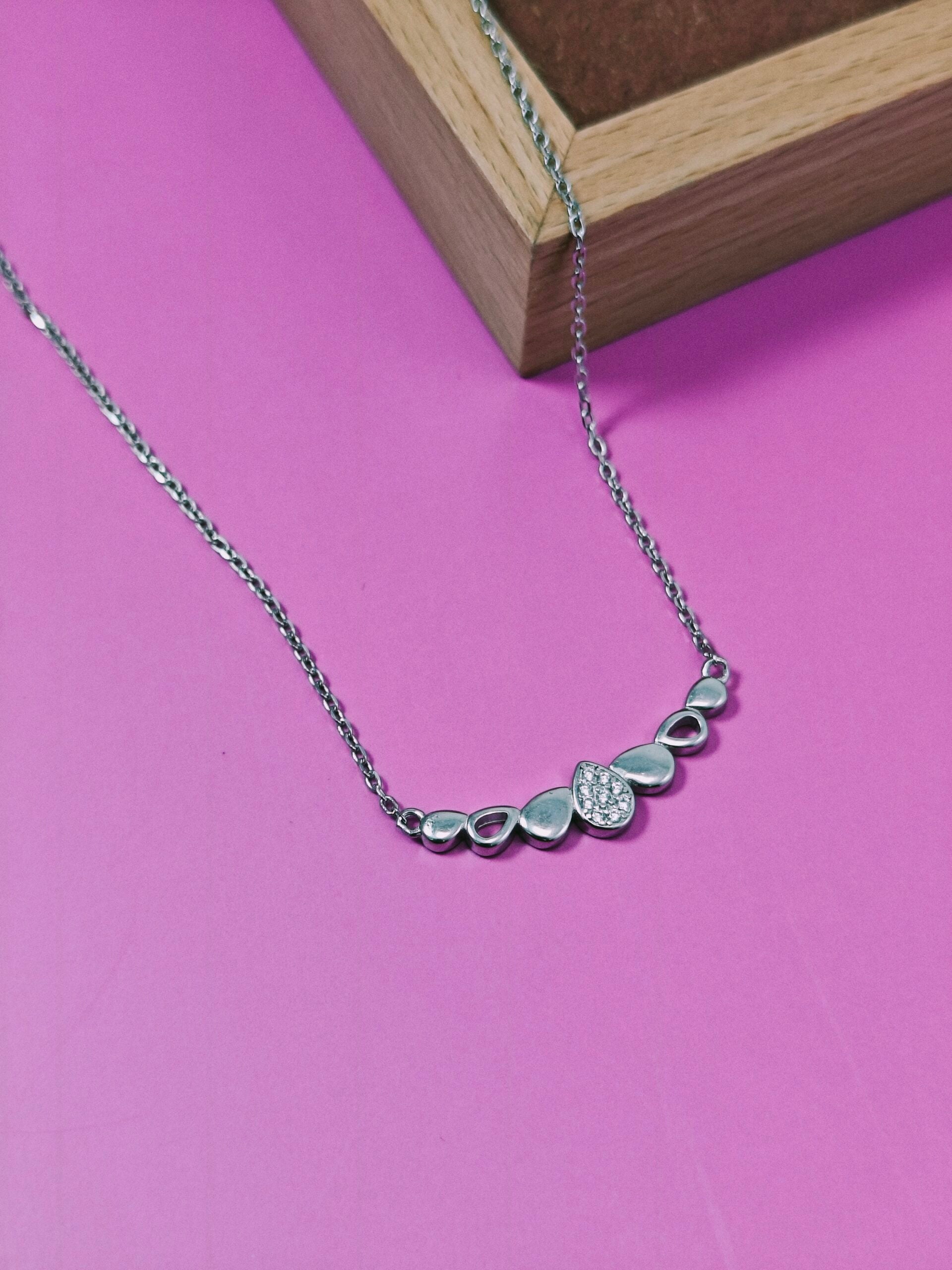 Silver necklace with a small diamond pendant on a pink background