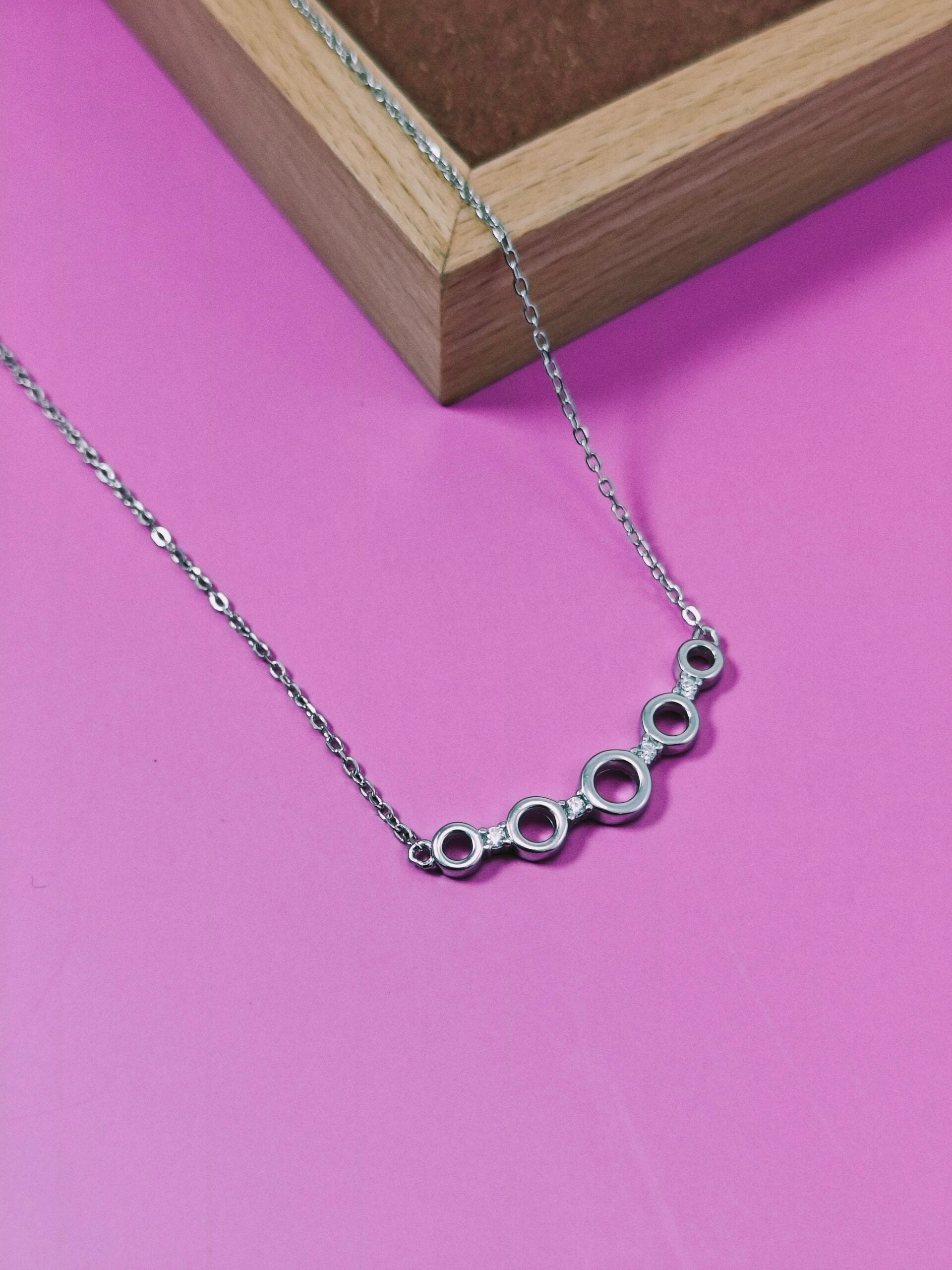 Silver necklace with circular links on a pink background