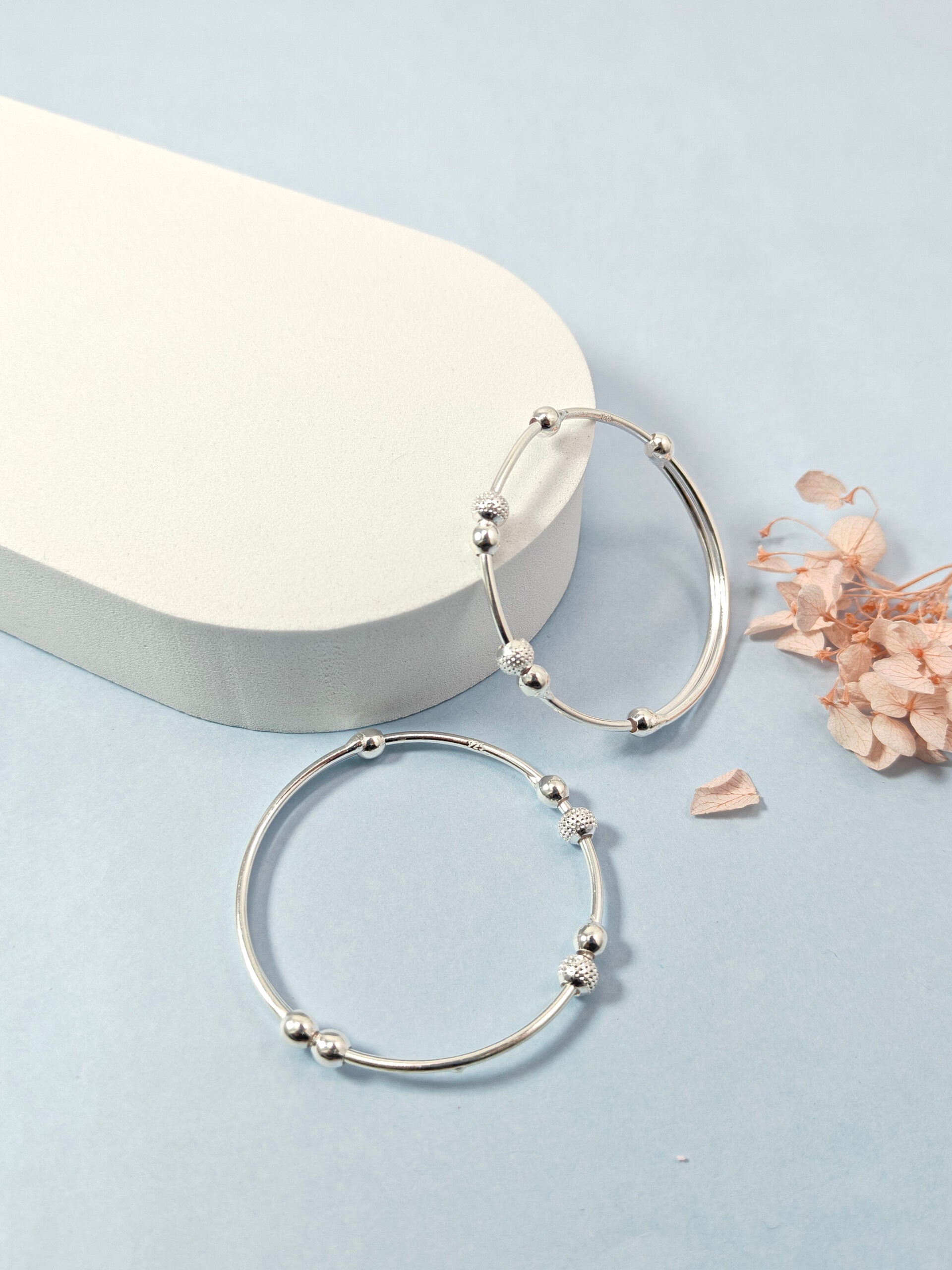 Silver hoop earrings on a light blue background with a white stone and dried flowers.