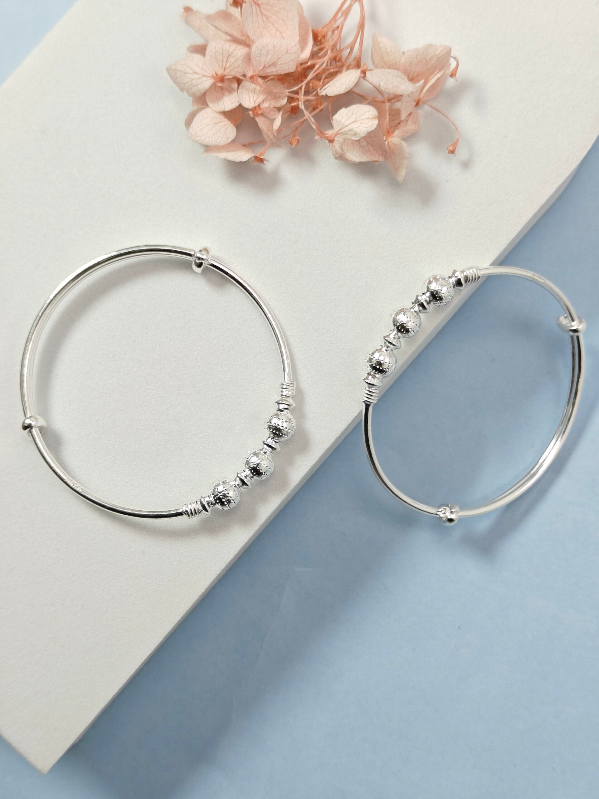 Silver hoop earrings with bead detailing on a light blue and white background with dried flowers.