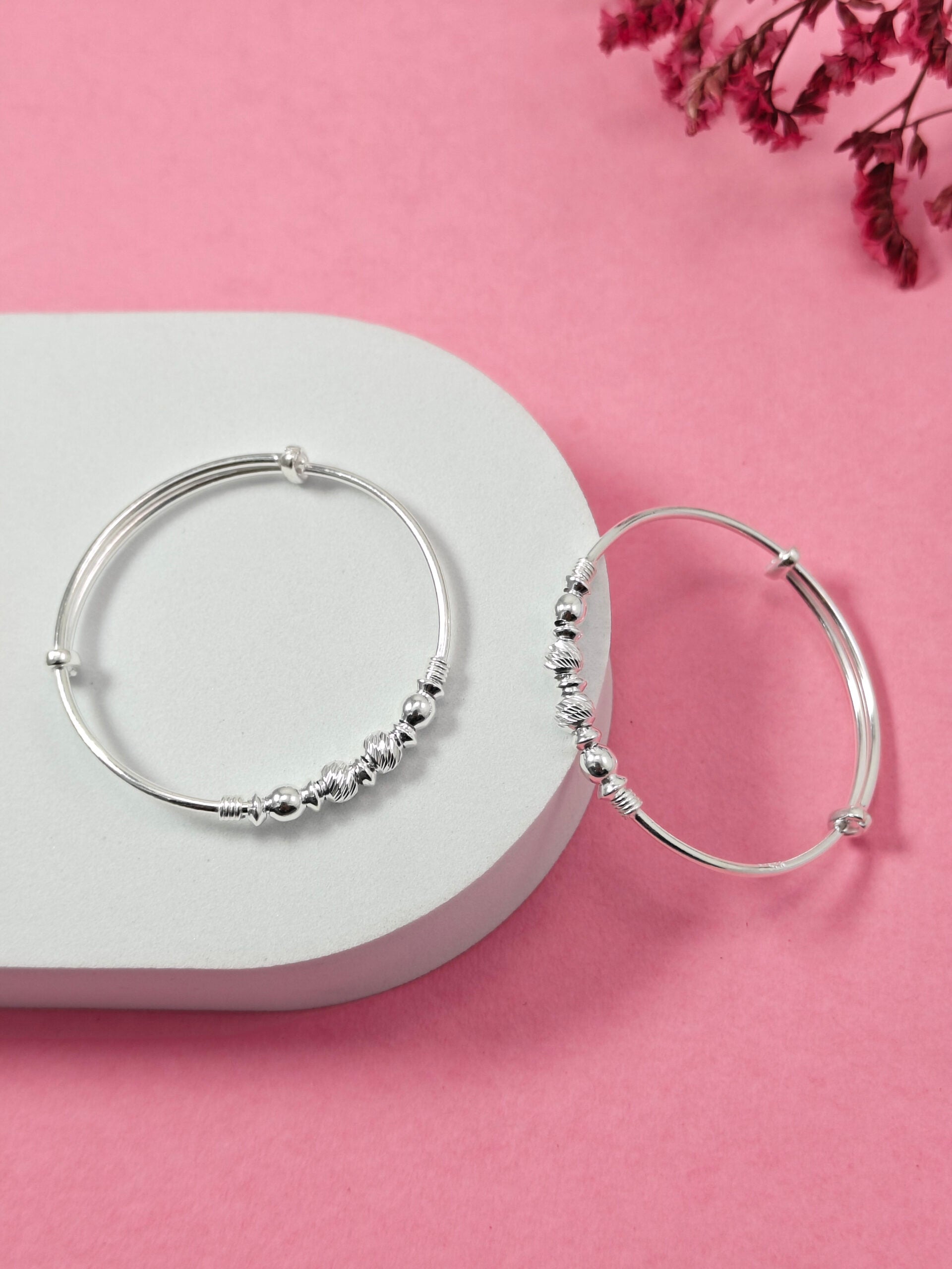 Silver hoop earrings with bead detailing on a white heart-shaped pad against a pink background