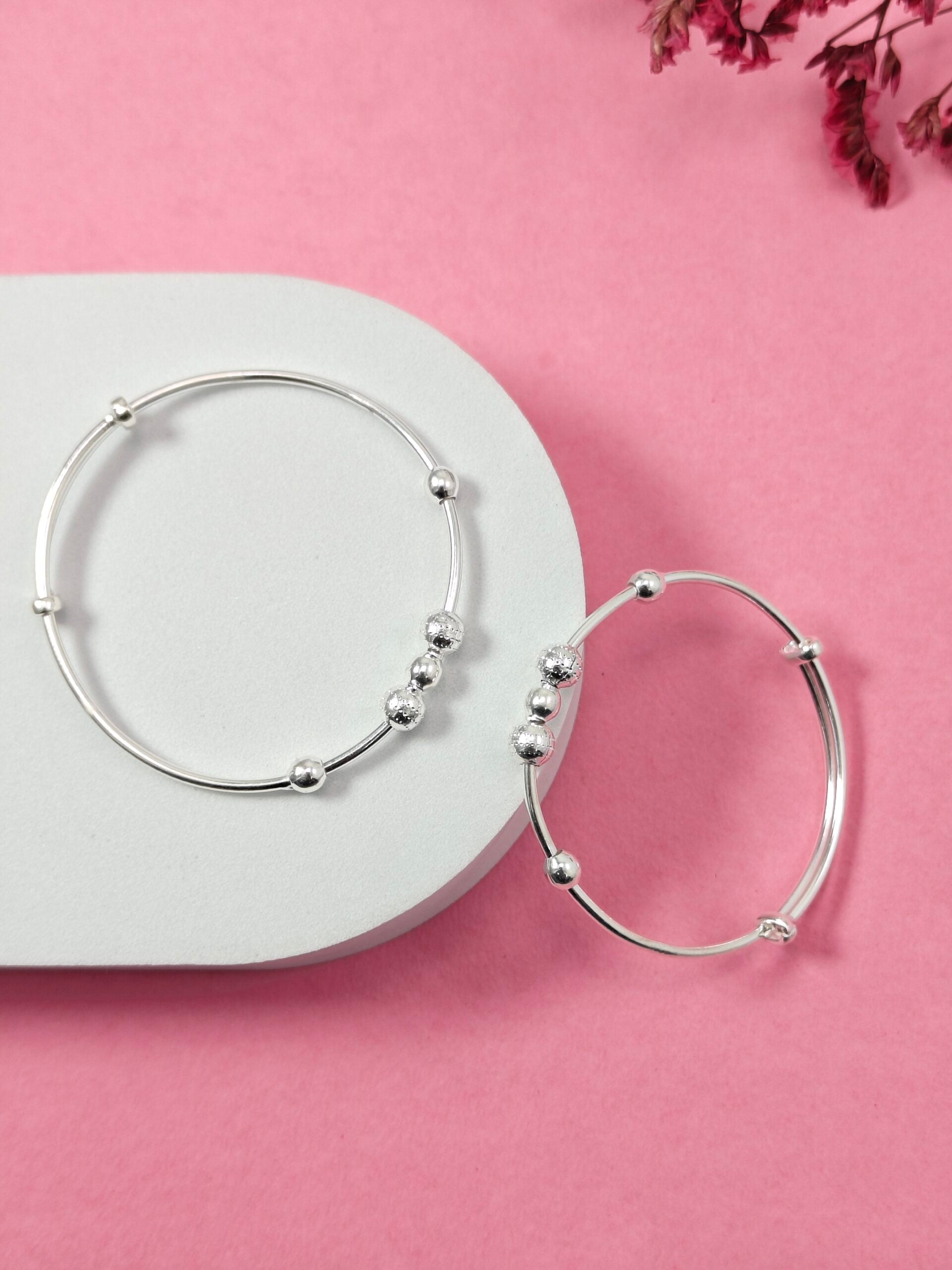 Silver hoop earrings on a white heart-shaped stand with pink flowers in the corner on a pink background