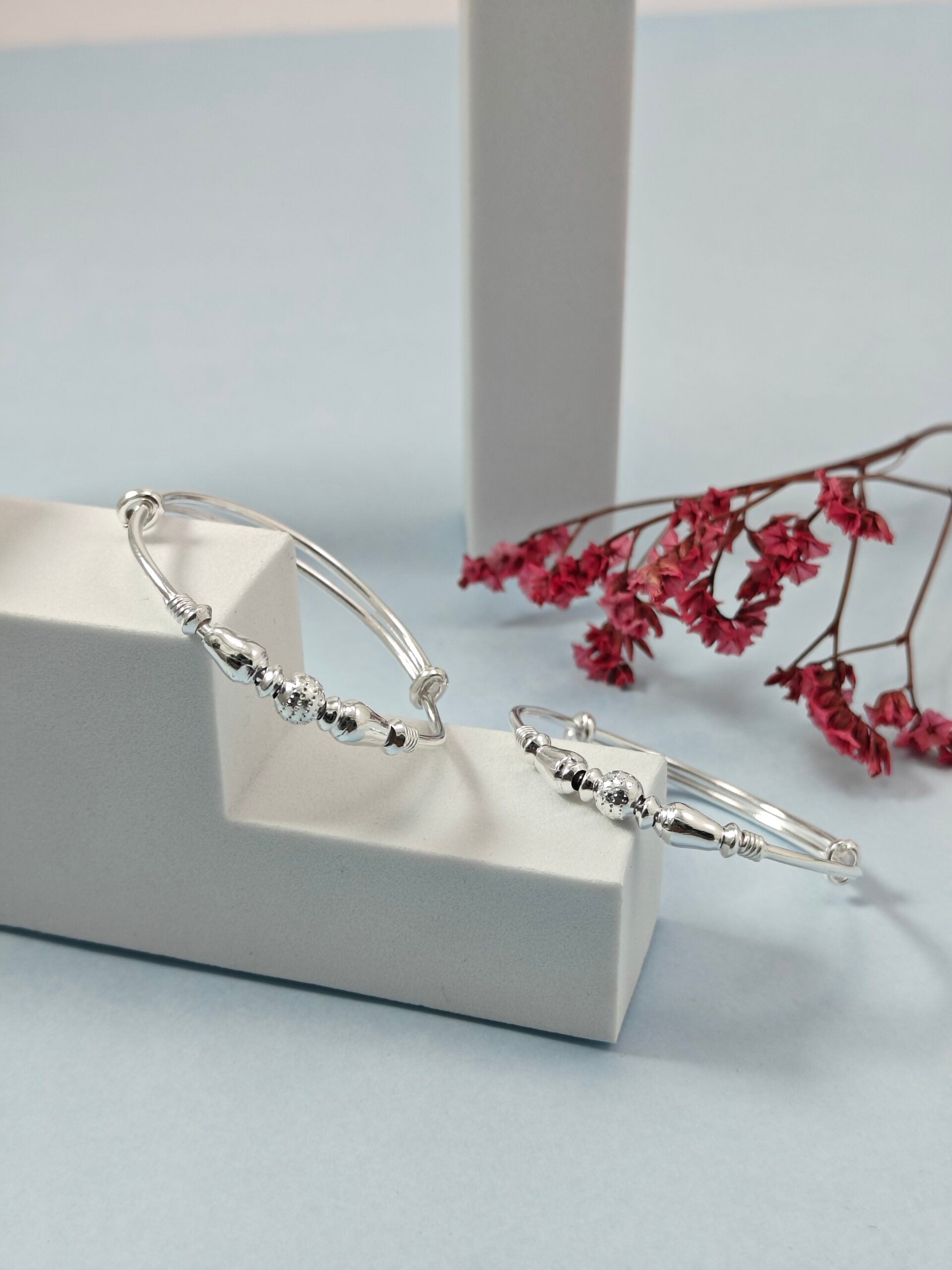 Silver bracelet on a white stand with pink flowers in the background