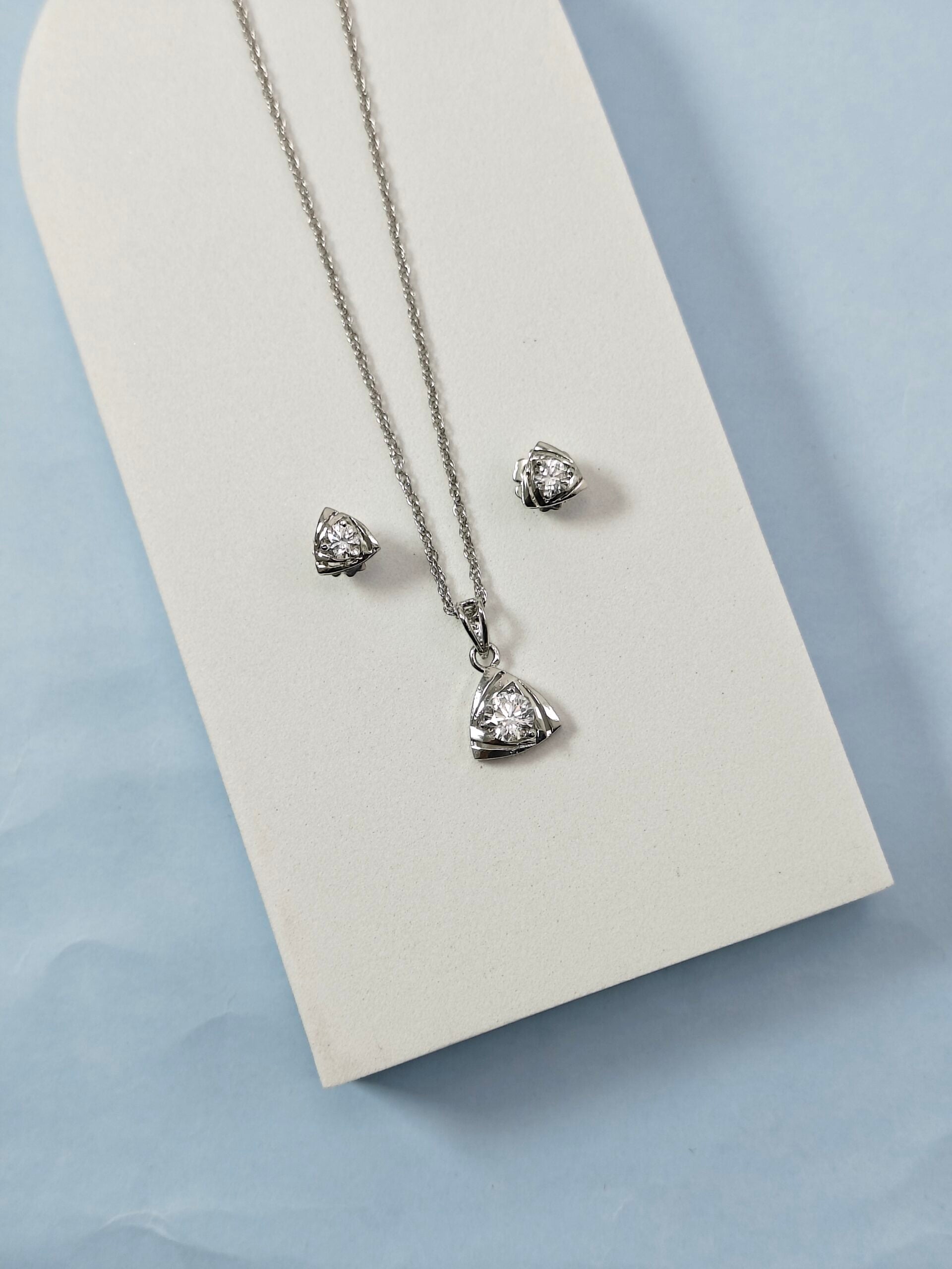 Silver necklace and earrings on a white card with a light blue background
