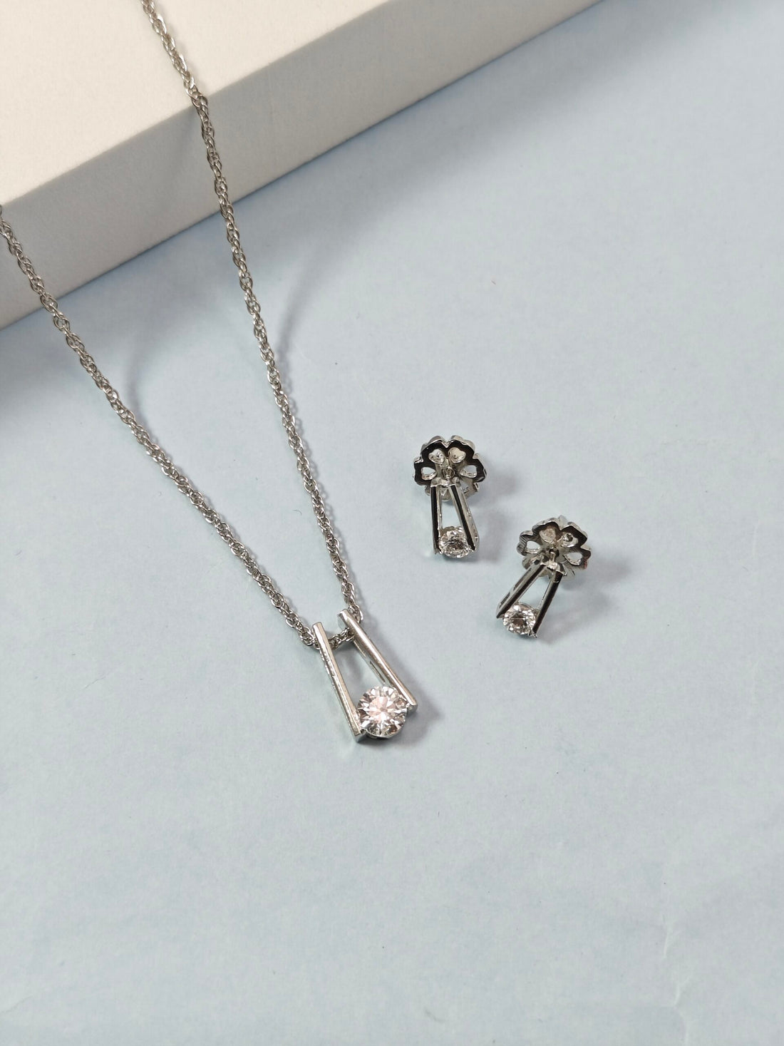 Silver necklace and earrings on a light blue surface