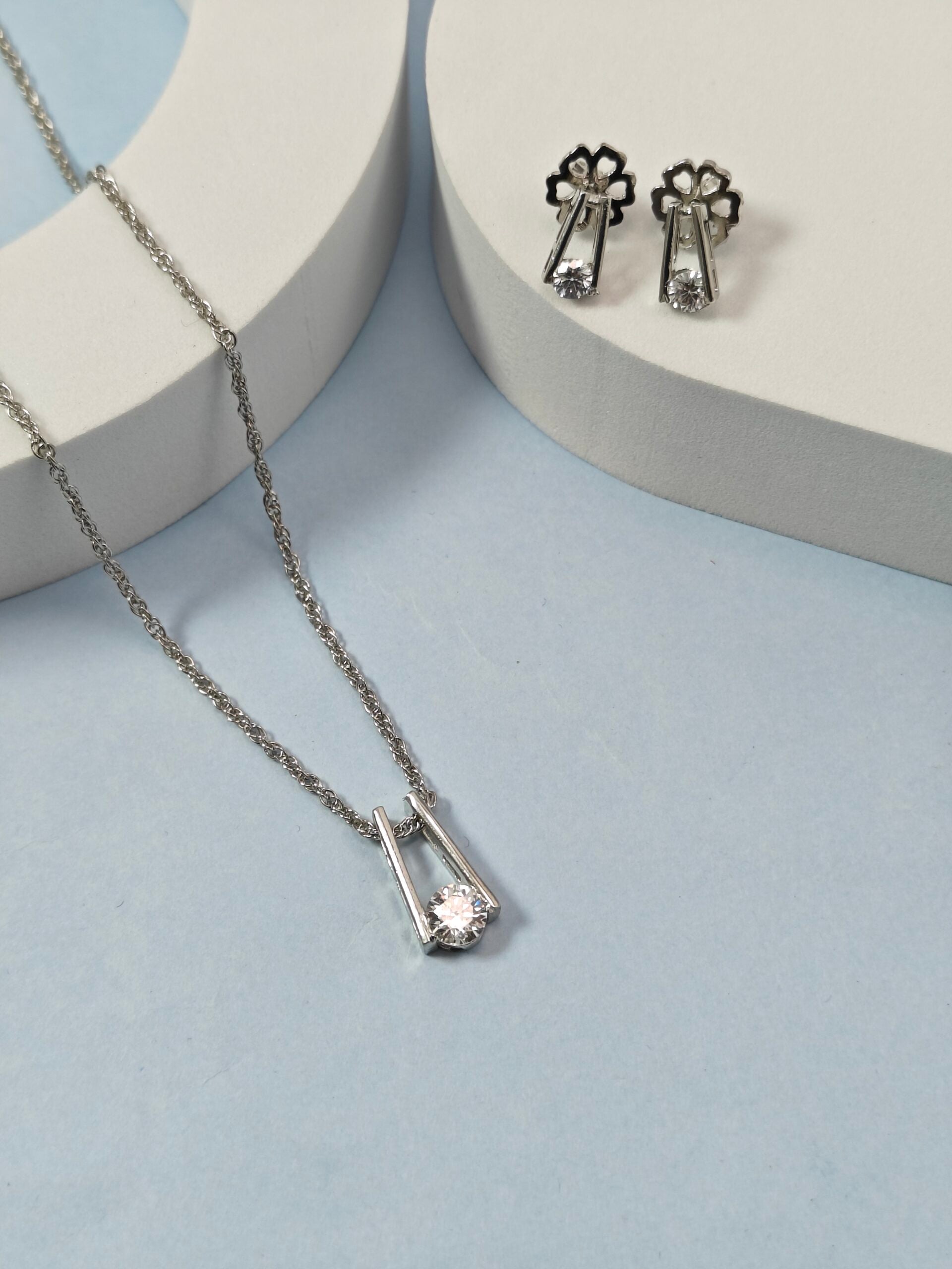 Silver necklace and earrings on a light blue background