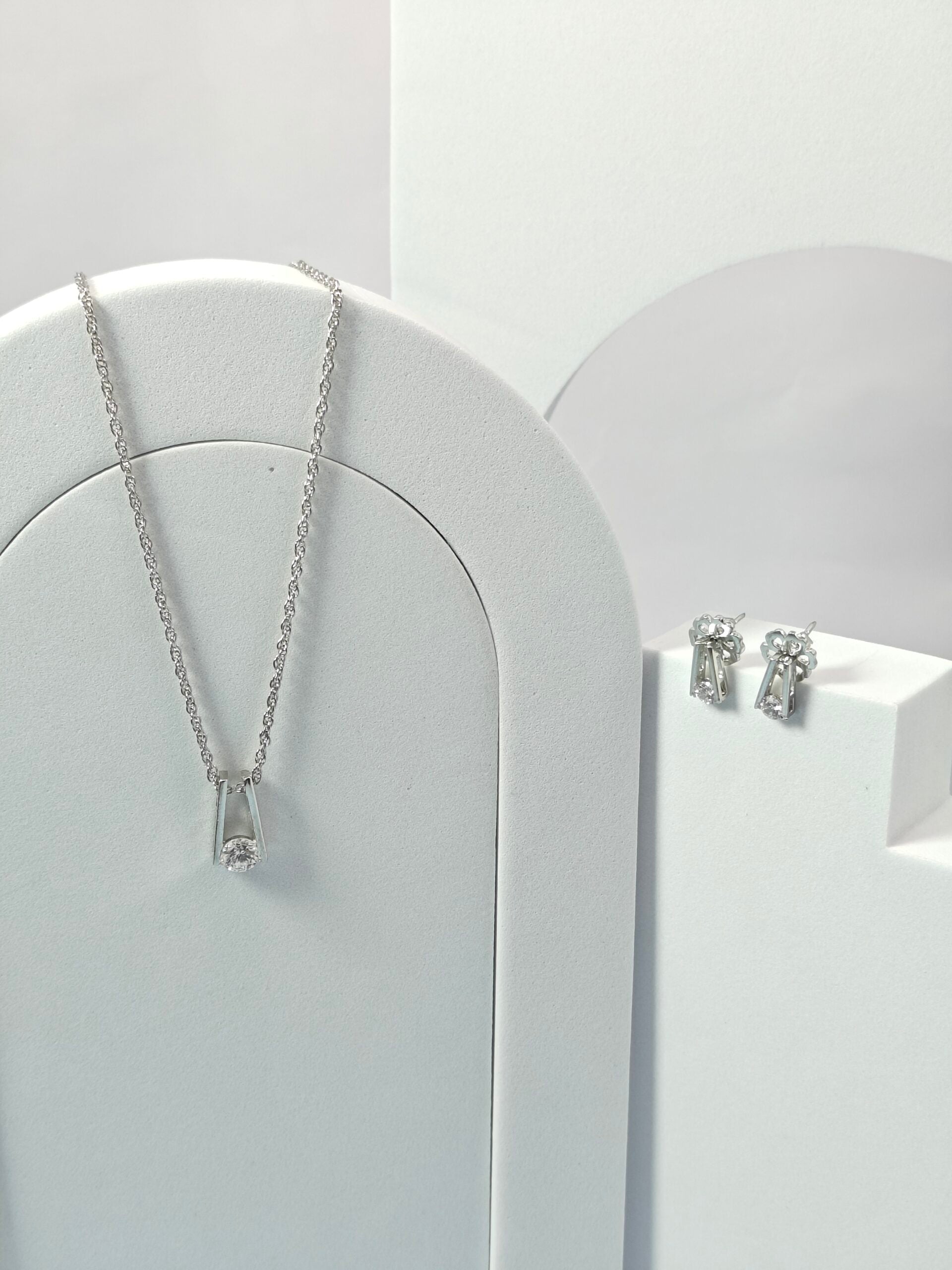 Silver necklace and earrings on a white stand against a light gray background