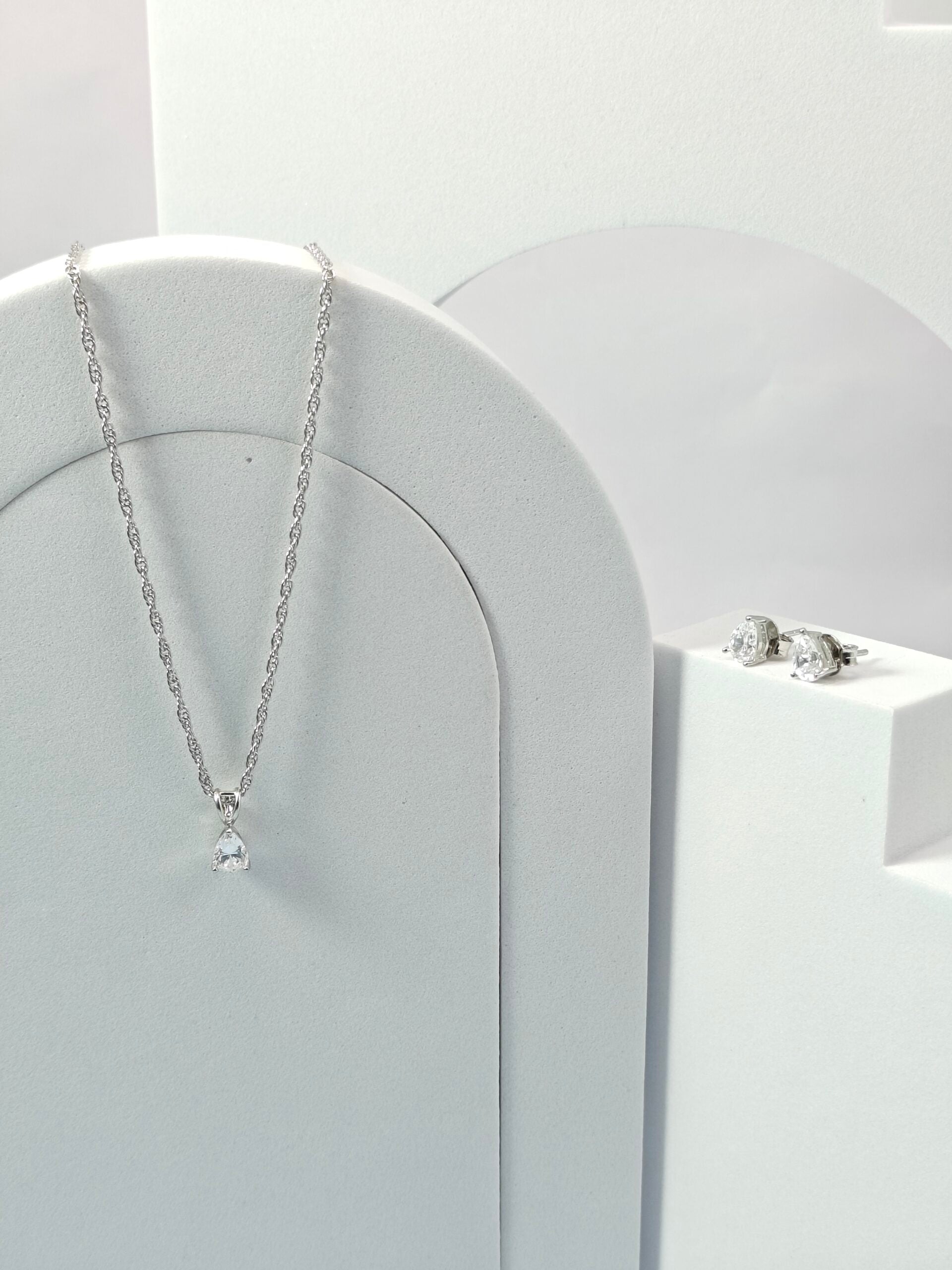 Silver necklace and earrings on a white stand with a white background