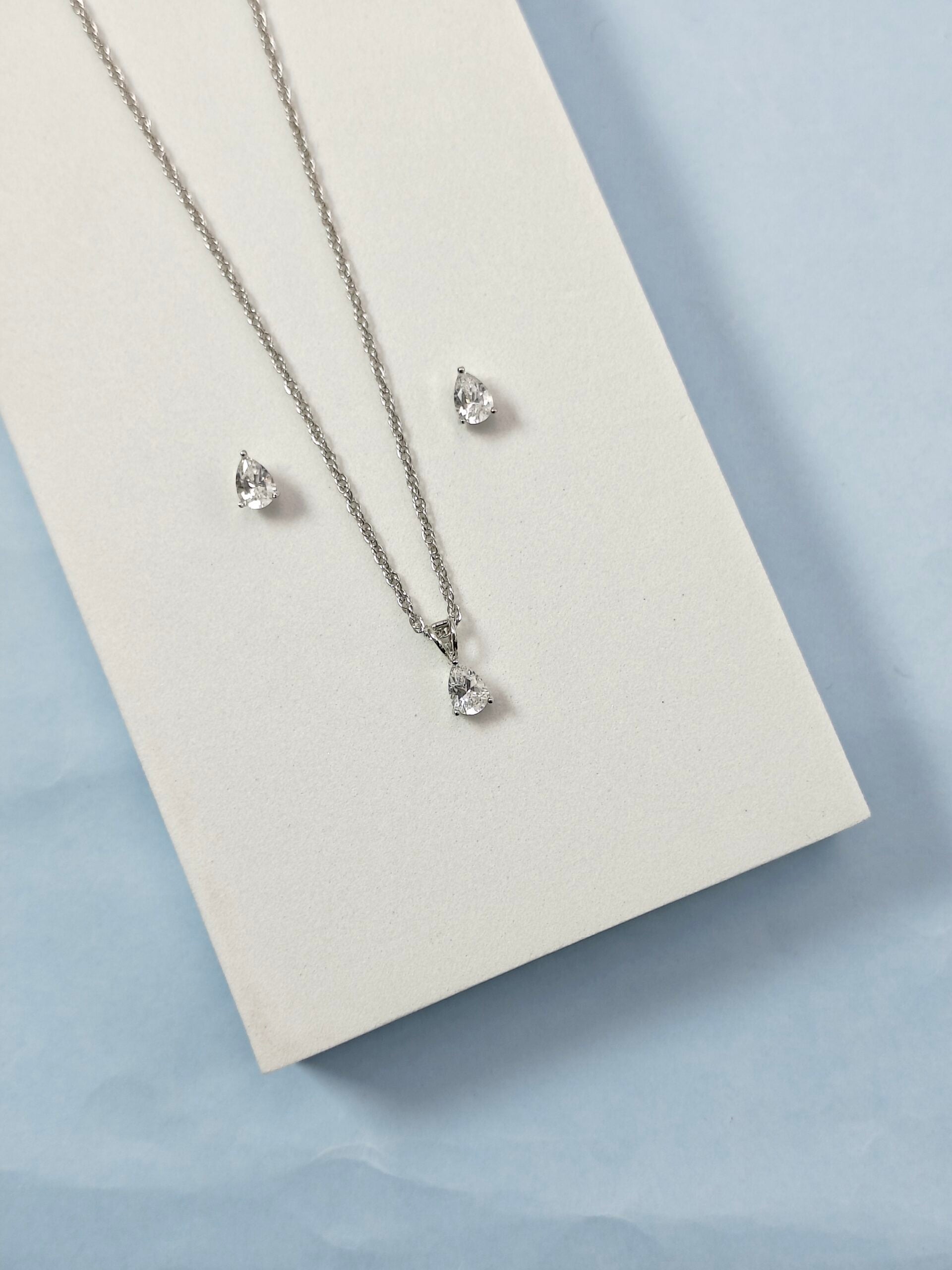 Silver necklace and earrings on a light gray card with a light blue background