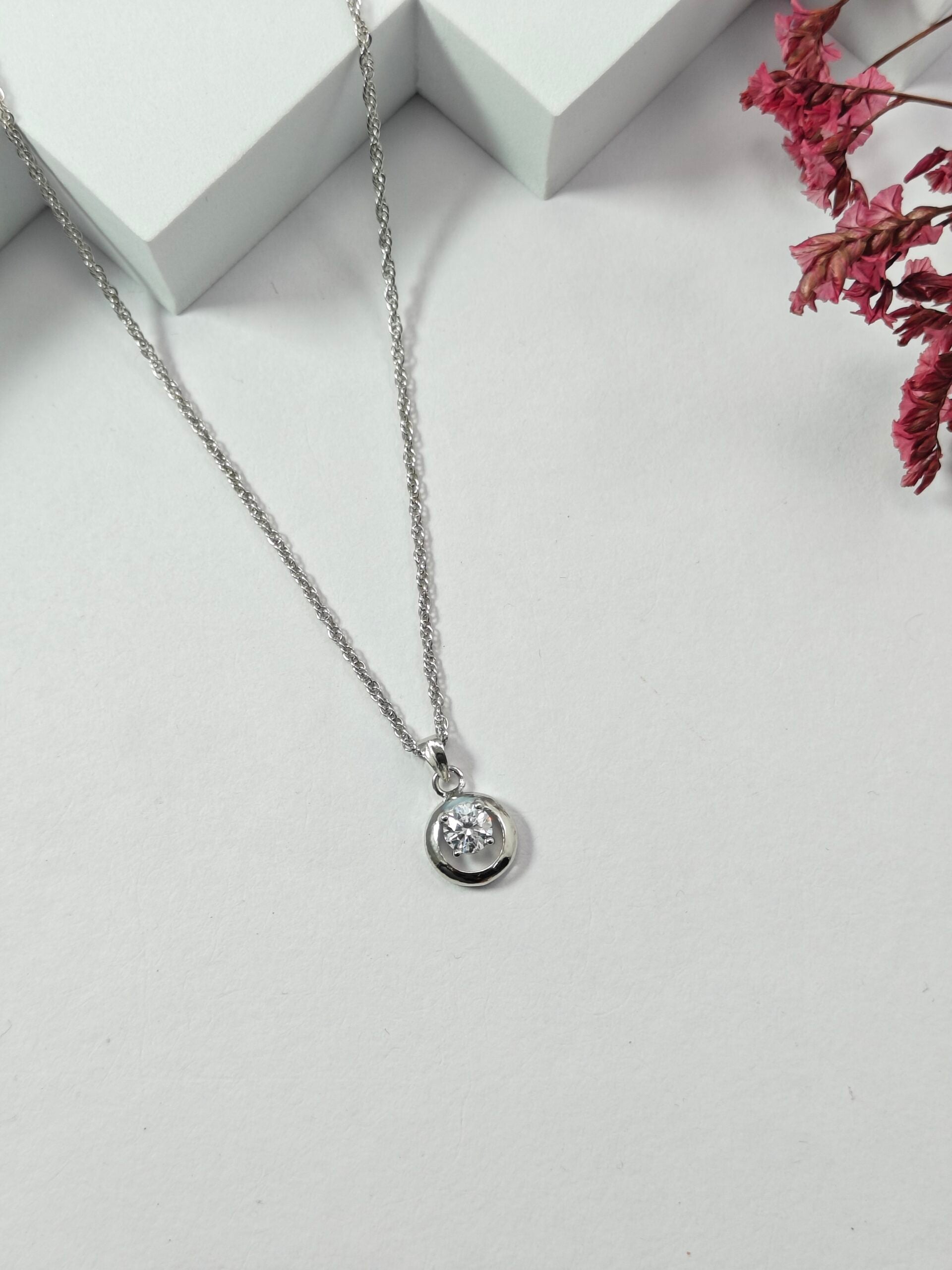 Silver necklace with a pendant on a light gray surface with pink flowers in the corner.