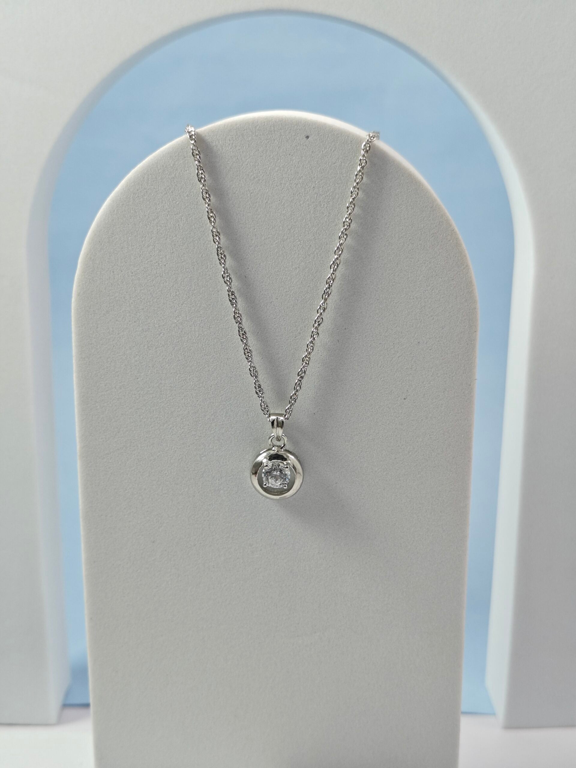 Silver necklace with a pendant on a gray stand against a light blue and white background
