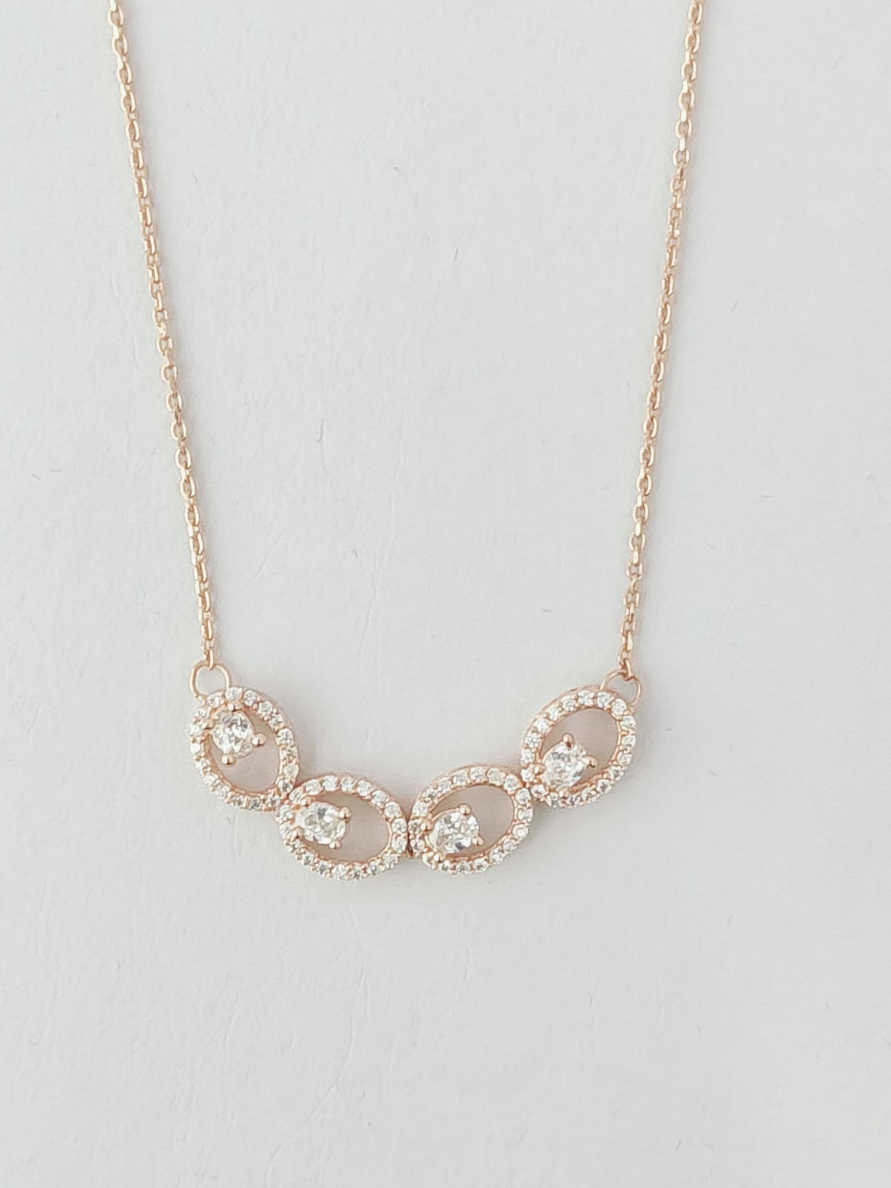 Rose gold necklace with circular pendants on a light gray background