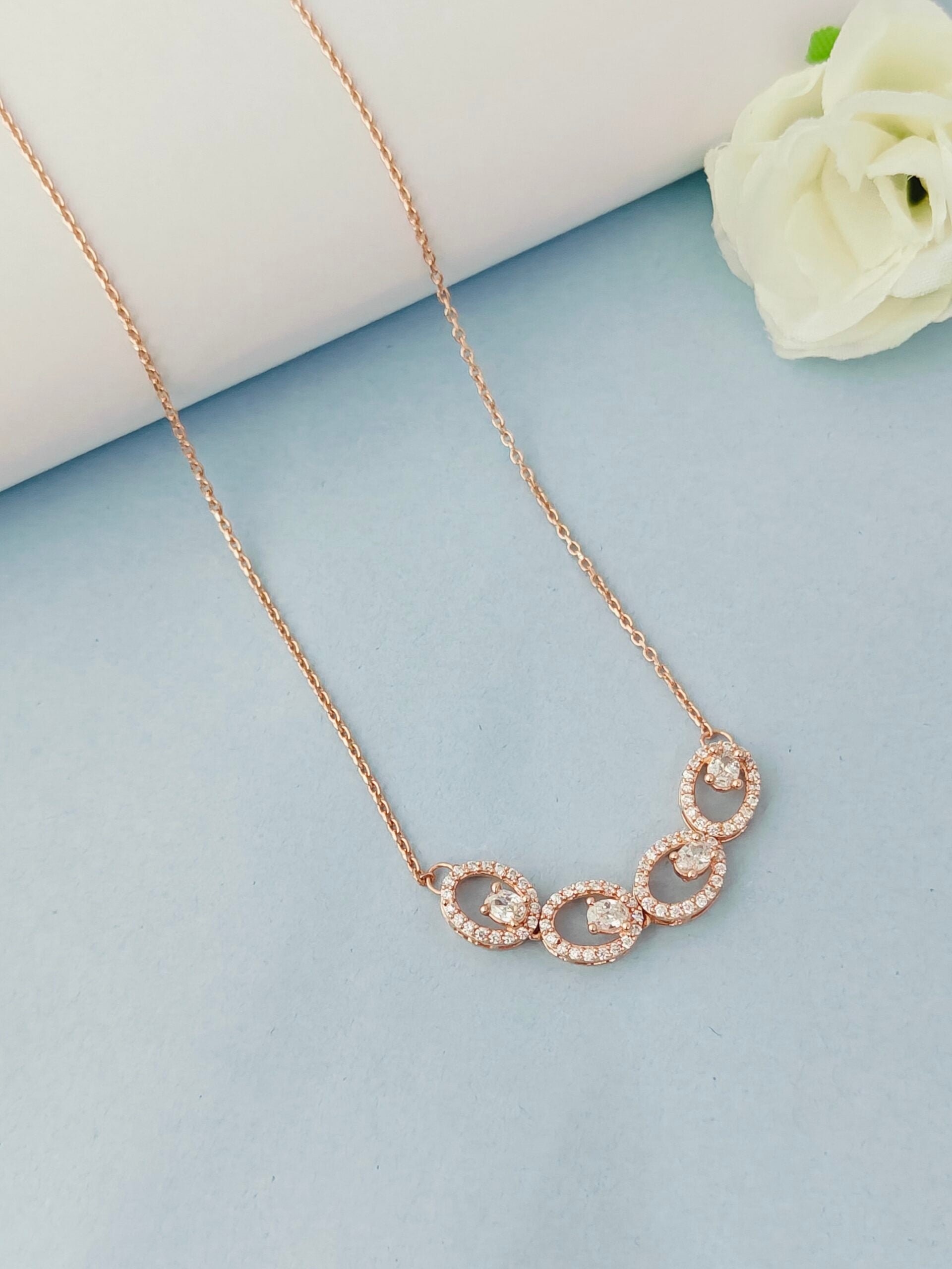 Rose gold necklace with circular pendants on a light blue surface with a white flower.
