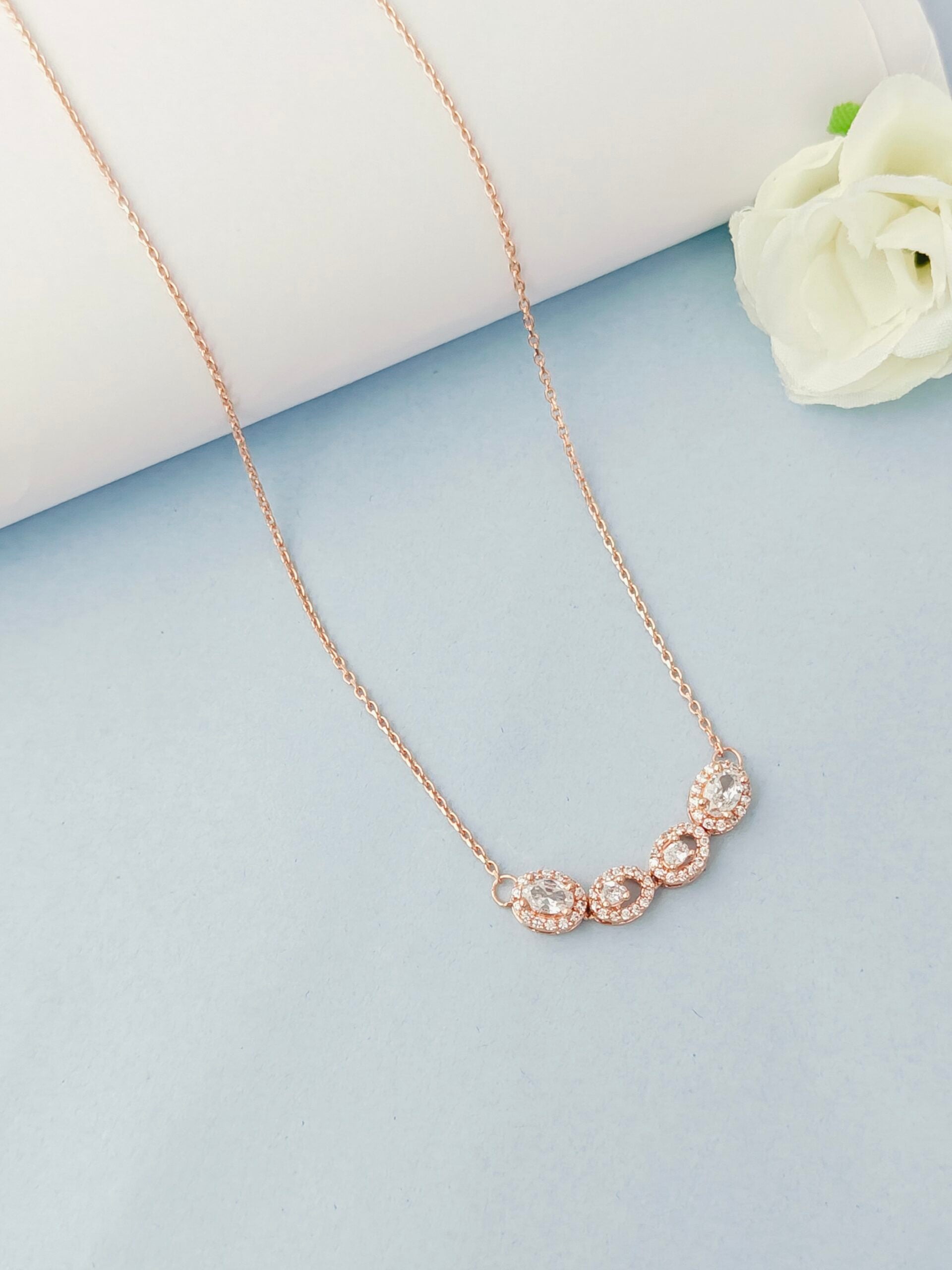 Rose gold necklace with floral design on a light blue surface with a white flower.