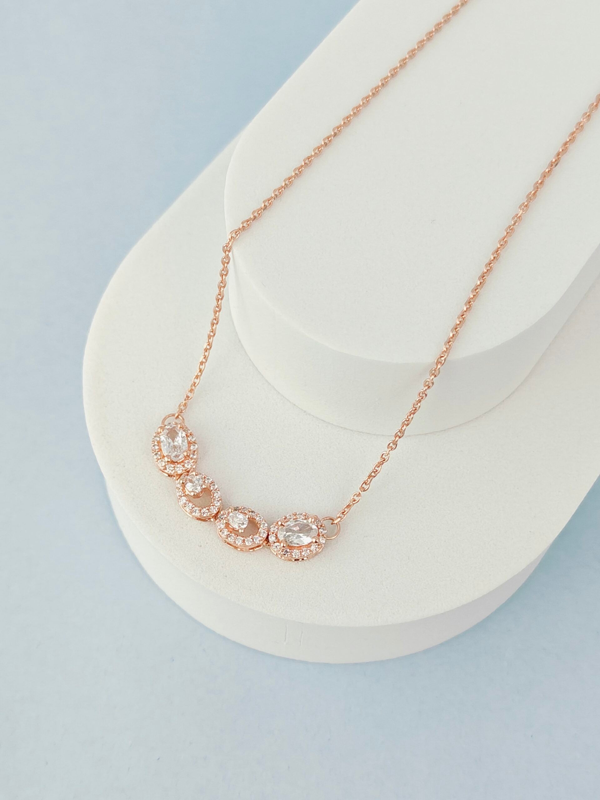 Rose gold necklace on a white stand with a light blue background
