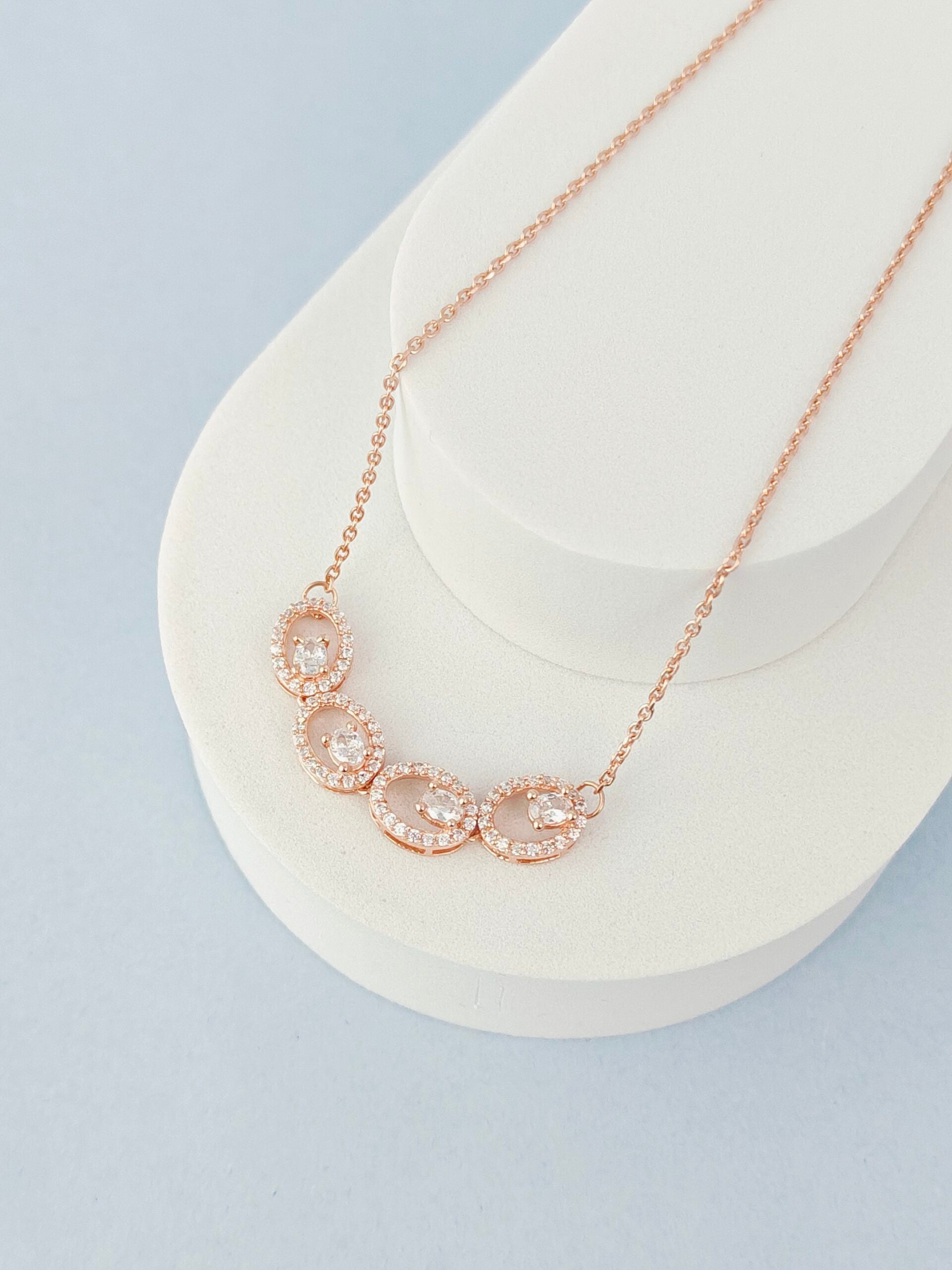 Rose gold necklace with pink gemstones on a white stand against a light blue background