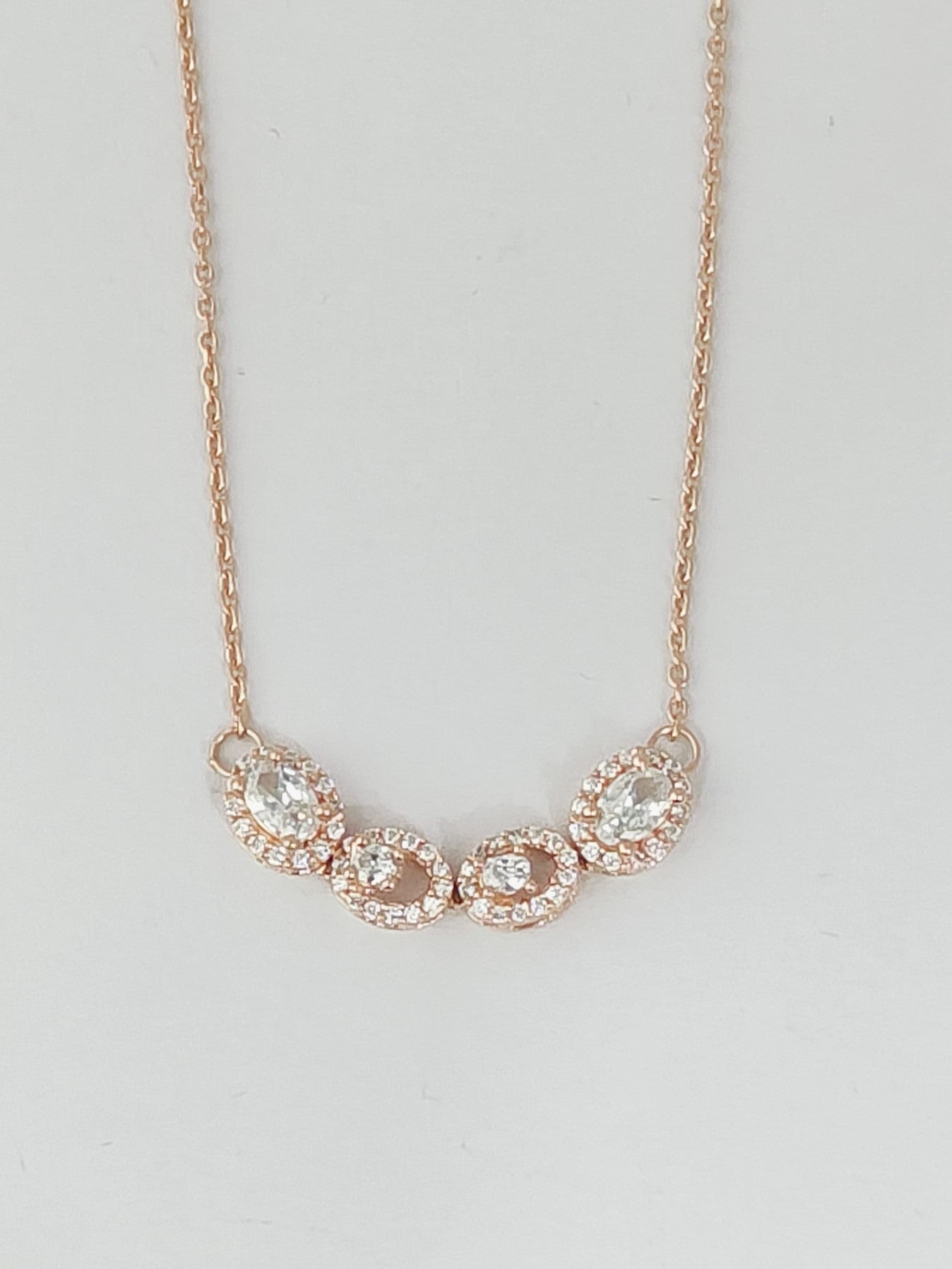 Rose gold necklace with clear stones on a light gray background
