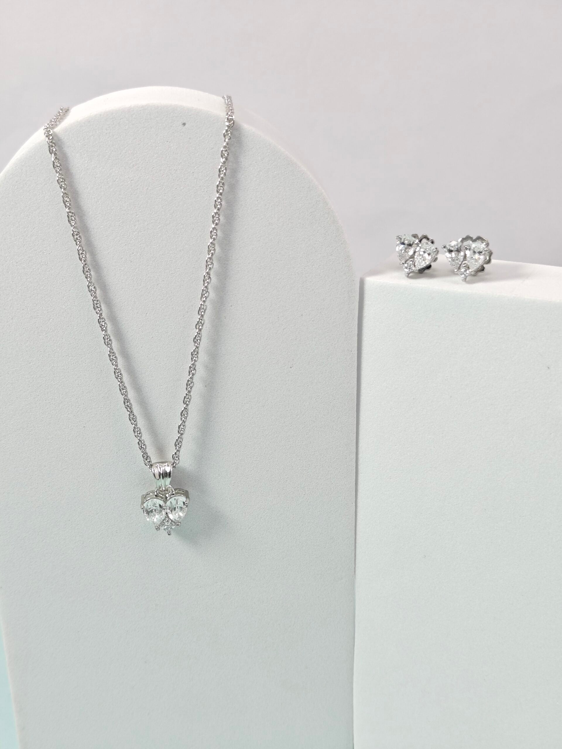 Silver necklace and earrings on a white stand with a light gray background