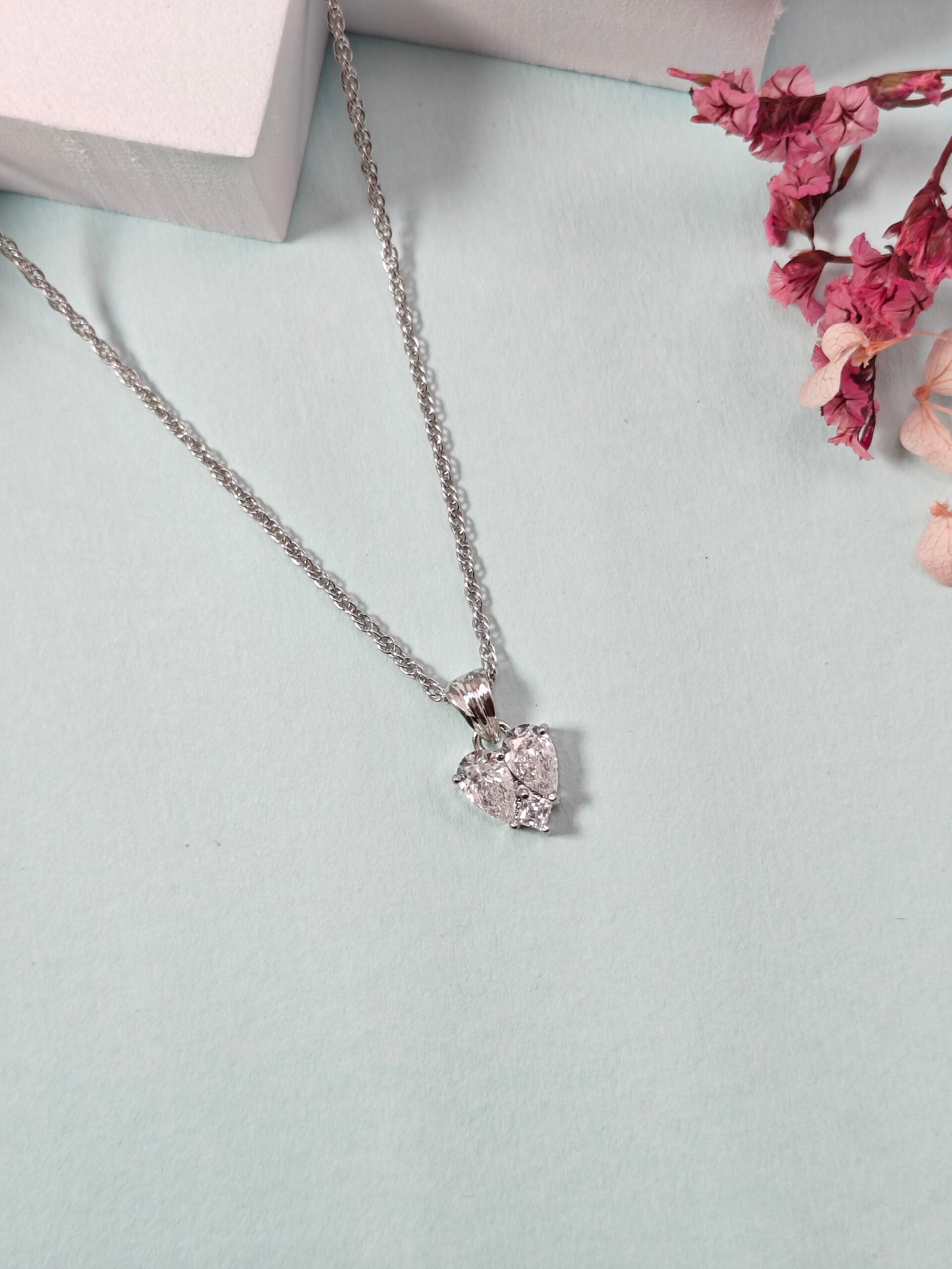 Silver necklace with a heart-shaped pendant on a light blue surface with pink flowers.