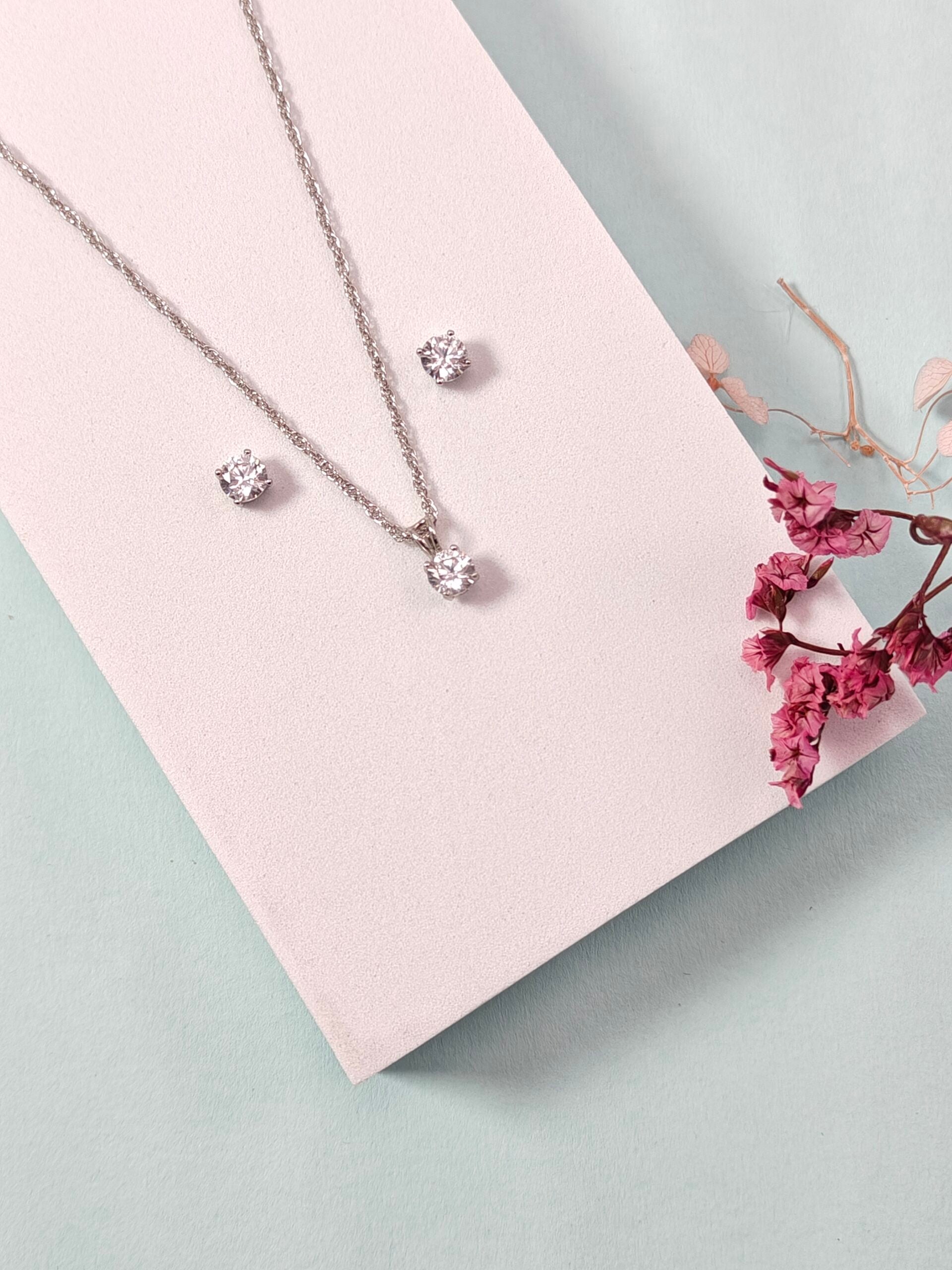 Silver jewelry set with necklace and earrings on a pink card with flowers.