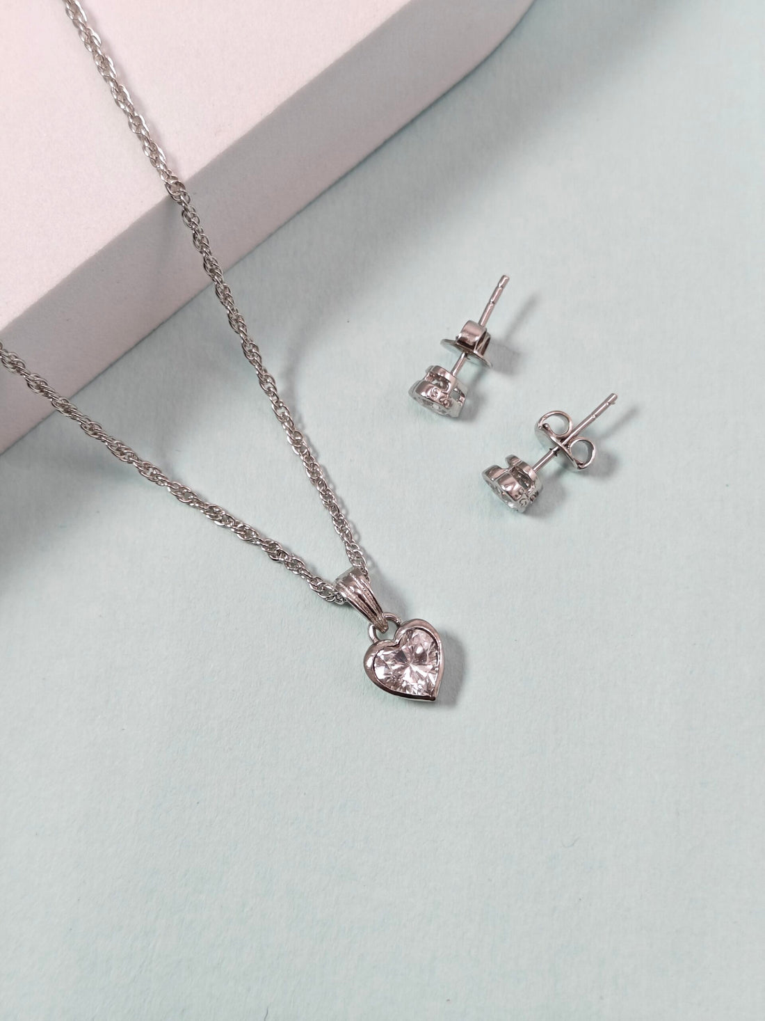 Silver heart-shaped necklace and earrings on a light green background