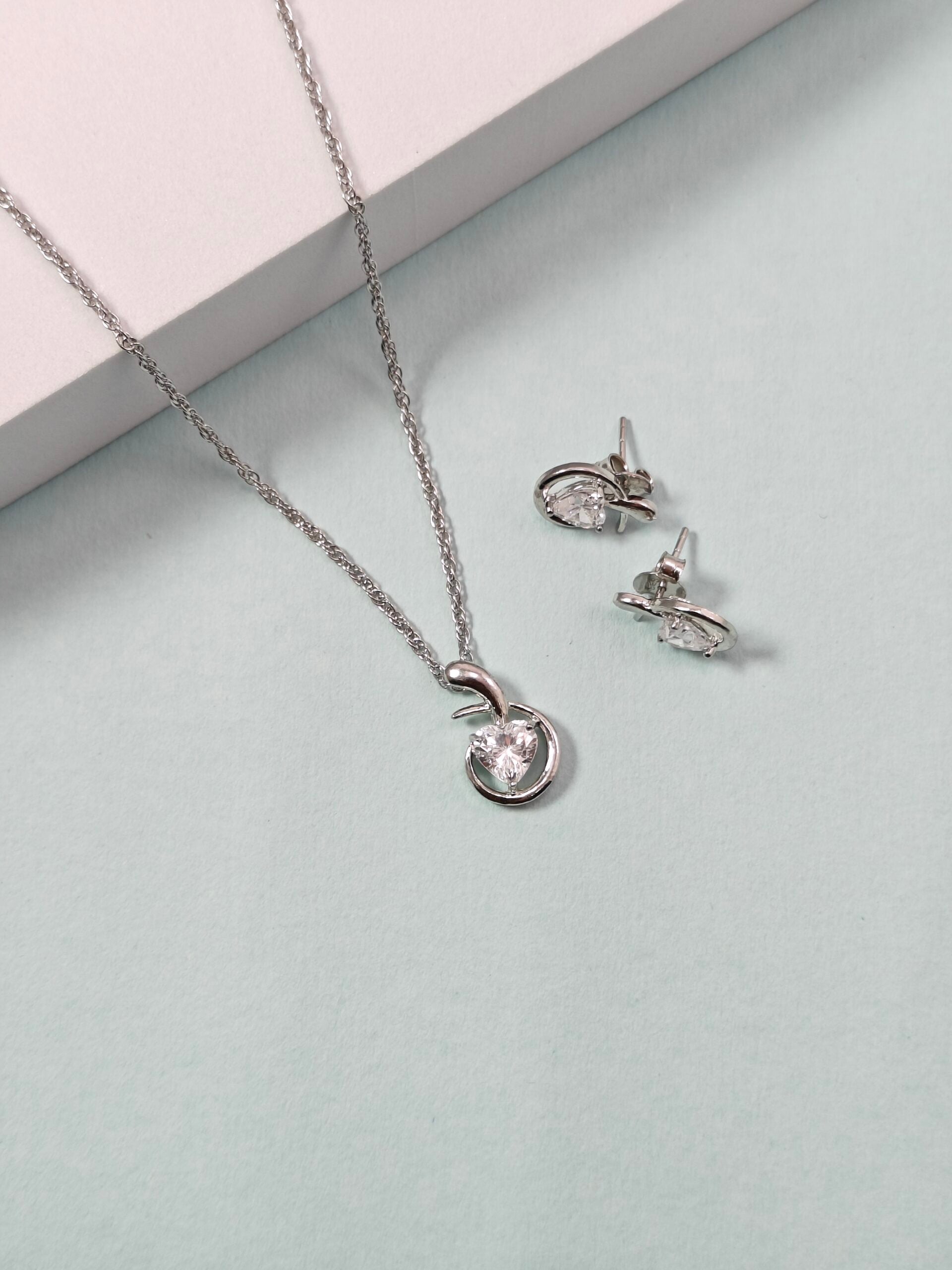 Silver necklace and earrings on a light gray surface