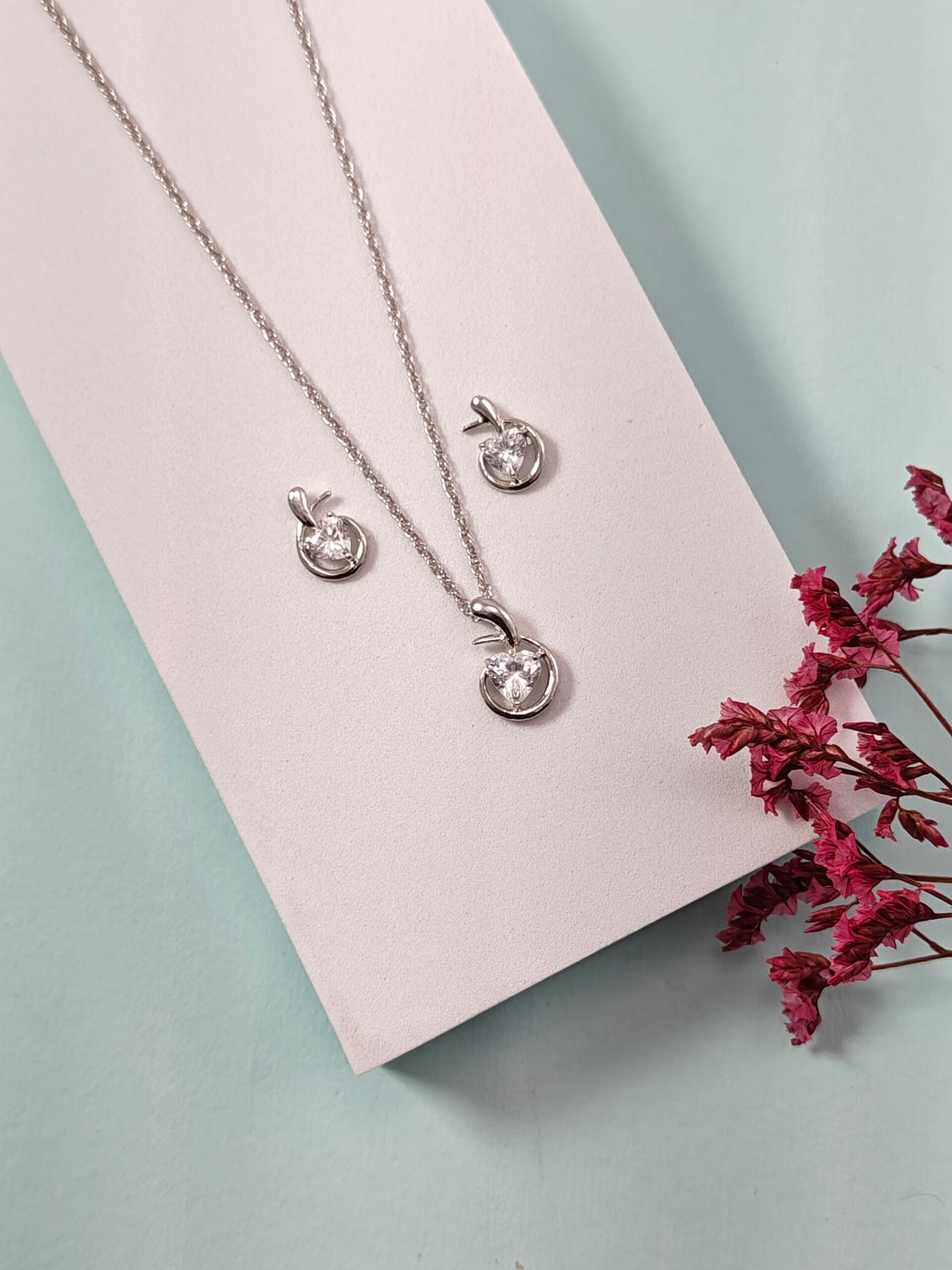 Silver necklace and earrings on a white card with dried pink flowers on a light blue background