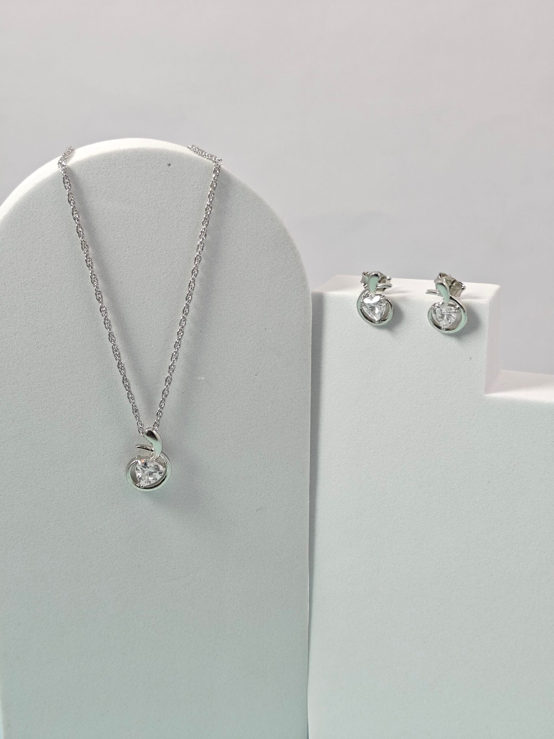 Silver necklace and earrings on a gray stand with a light gray background